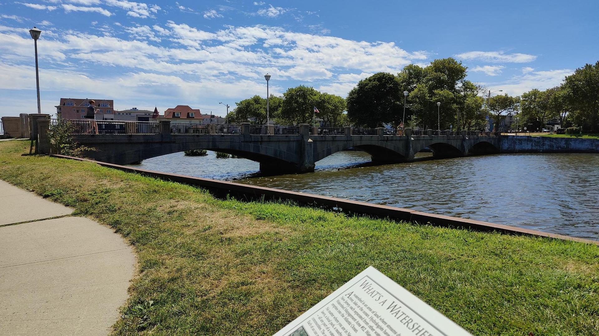 Sunny view of a stone bridge over a river with urban buildings.