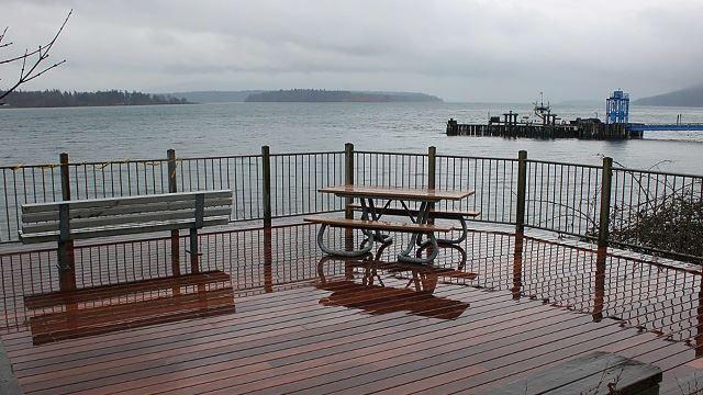 Wet wooden deck with a bench and picnic table overlooking a cloudy bay.