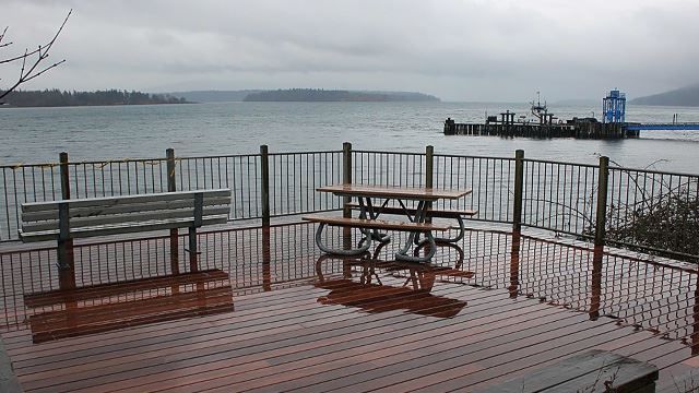 Wet wooden deck with a bench and picnic table overlooking a cloudy bay. - Lummi Island Overlook – Ferndale Road loop from Haxton Way at Cagey Rd