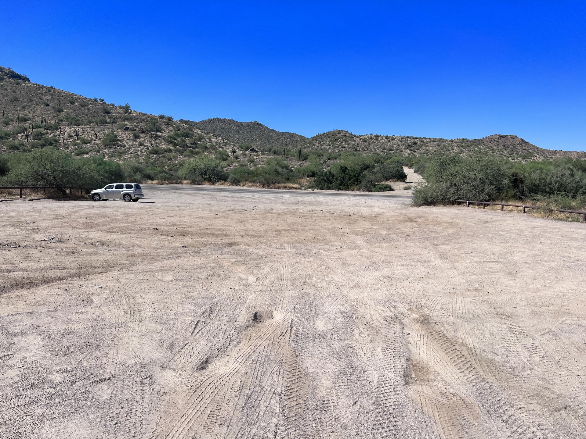 Large dirt parking lot with one white SUV and distant desert hills.