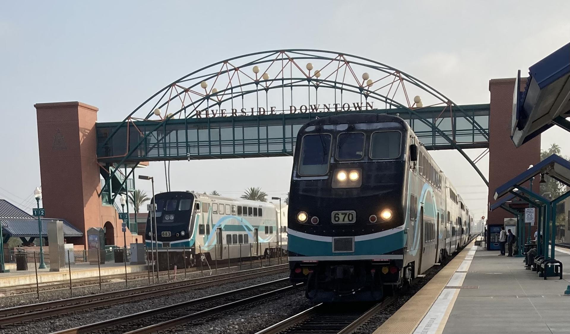Two passenger trains at a station platform with an arched pedestrian bridge.