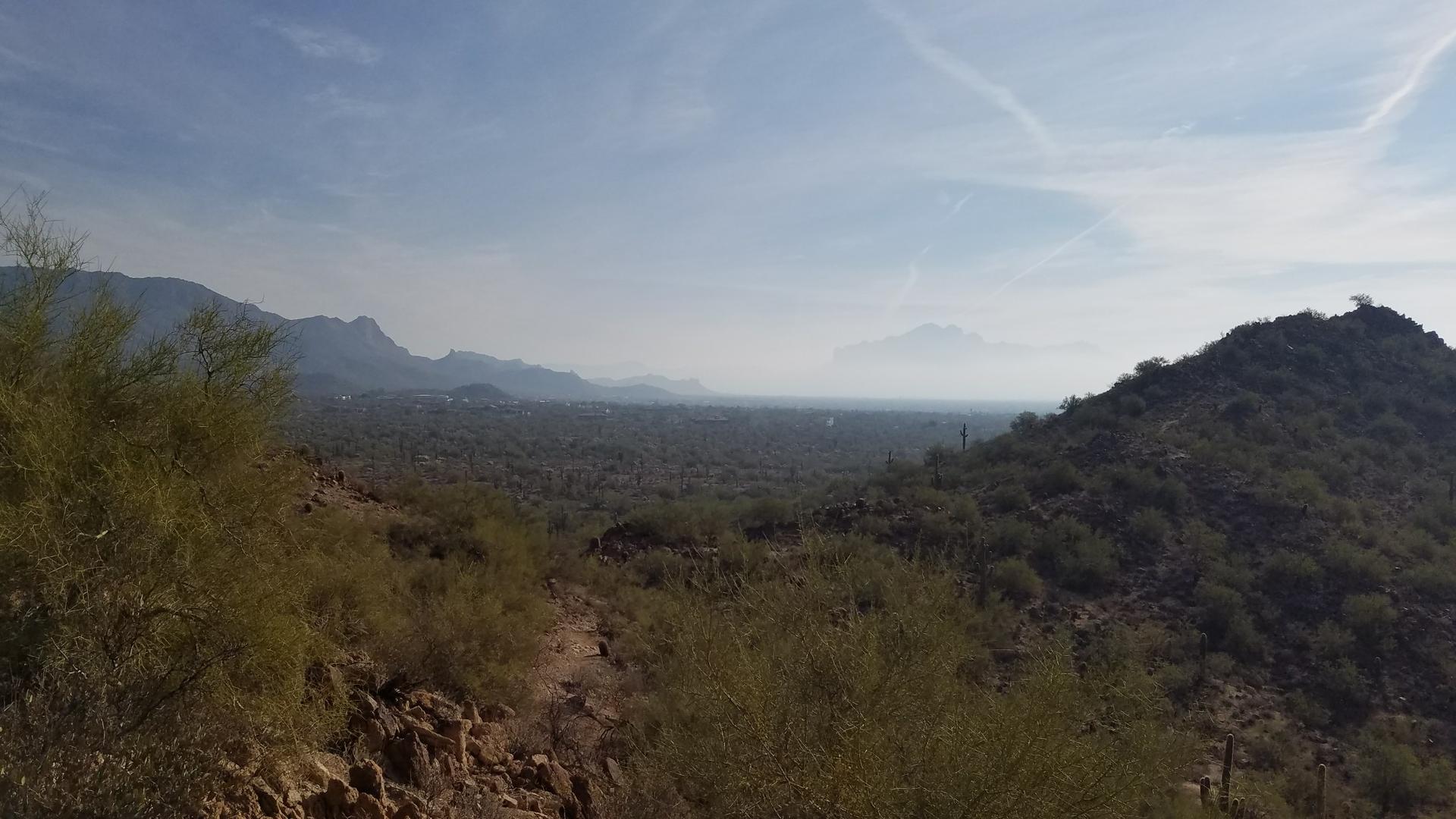 Expansive desert landscape with green hills, distant mountains, and a hazy sky.