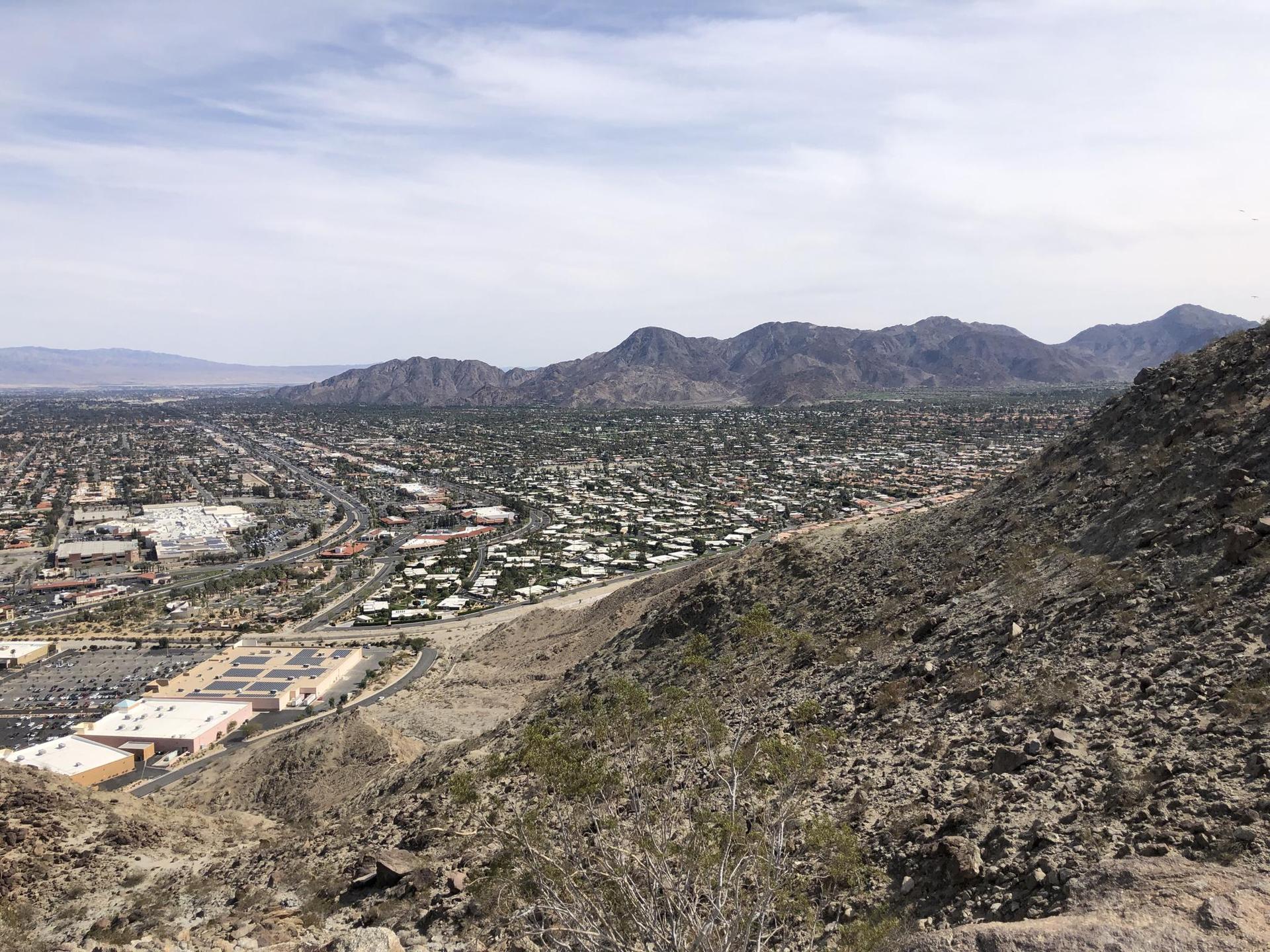 Overhead view of a sprawling city with mountains in the distance under a cloudy sky.