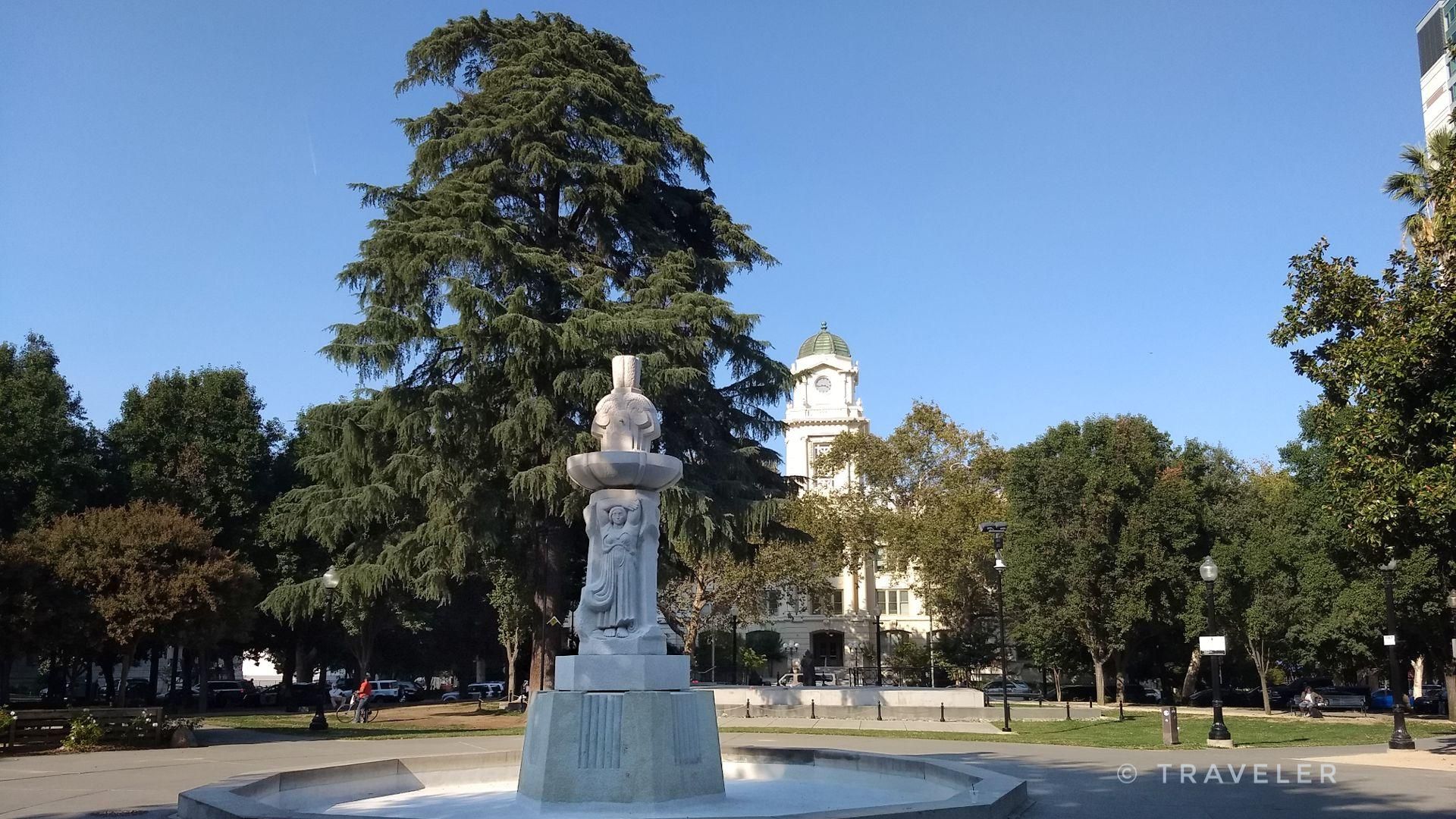 White stone fountain in a sunny park with large trees and a distant building. - Old Sacramento via Downtown Sacramento loop