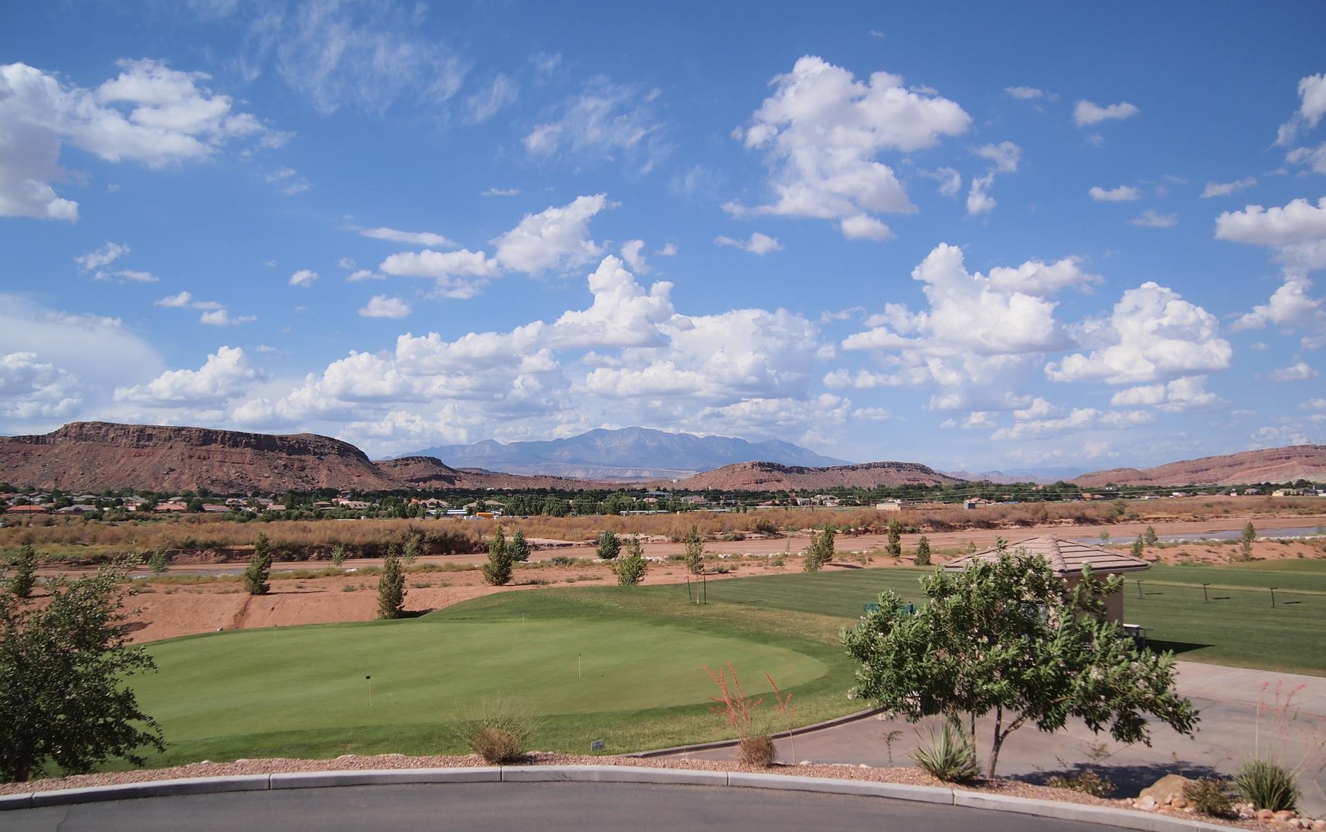 A sunny golf course with green fairways and distant mountains under a blue sky.