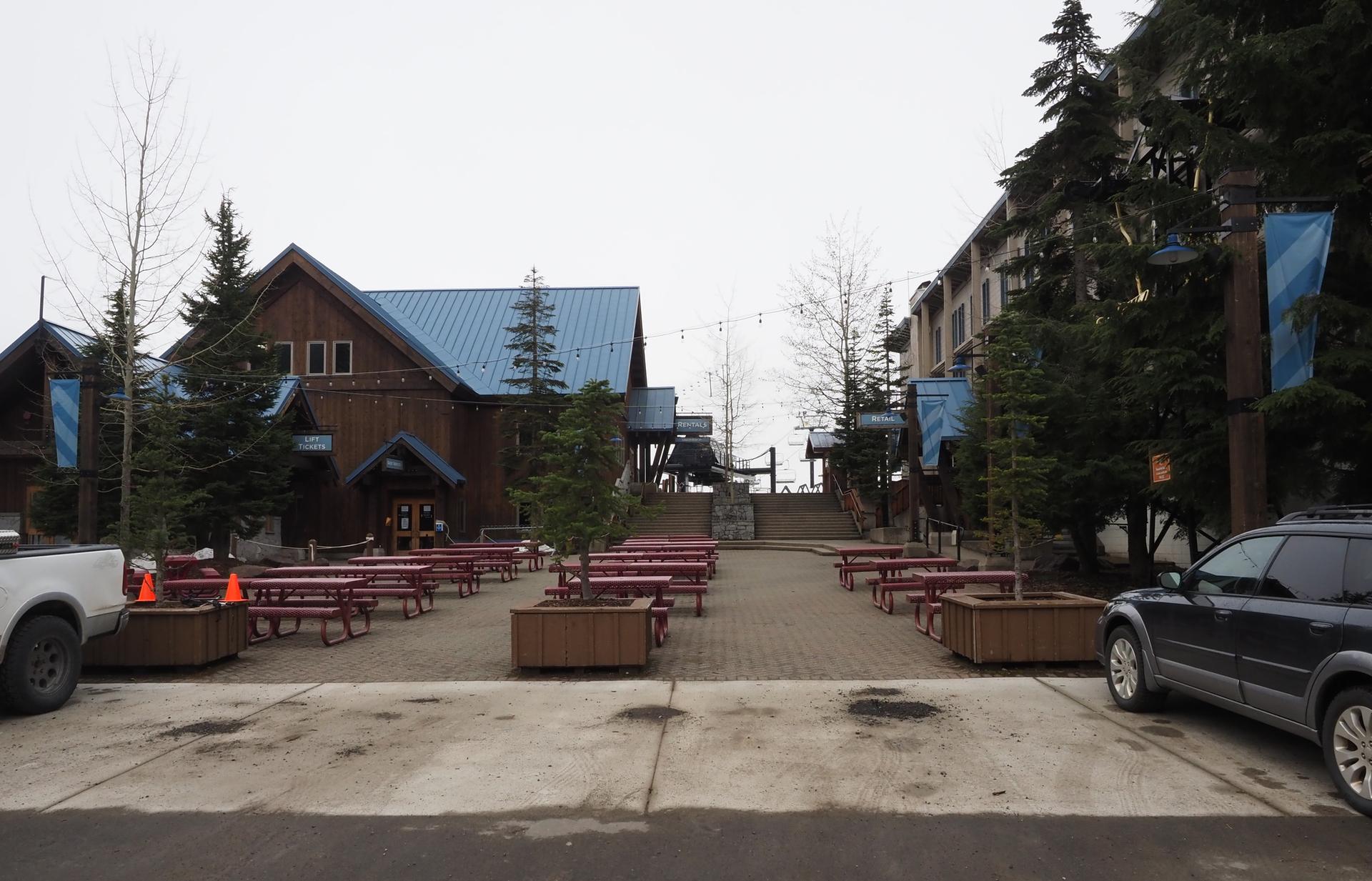 Overcast view of wooden buildings, empty picnic tables, and a paved area.
