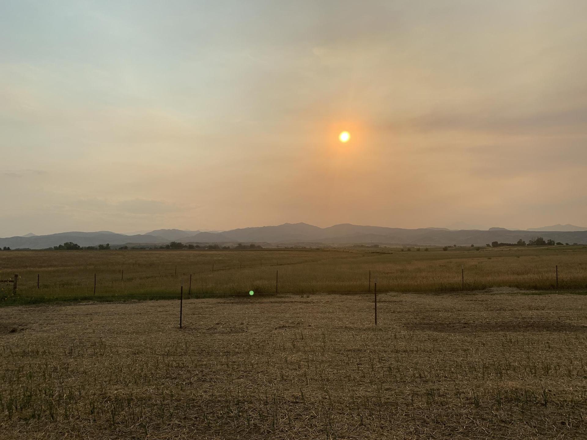 Hazy sunset over dry fields and distant mountains, with an orange sun.