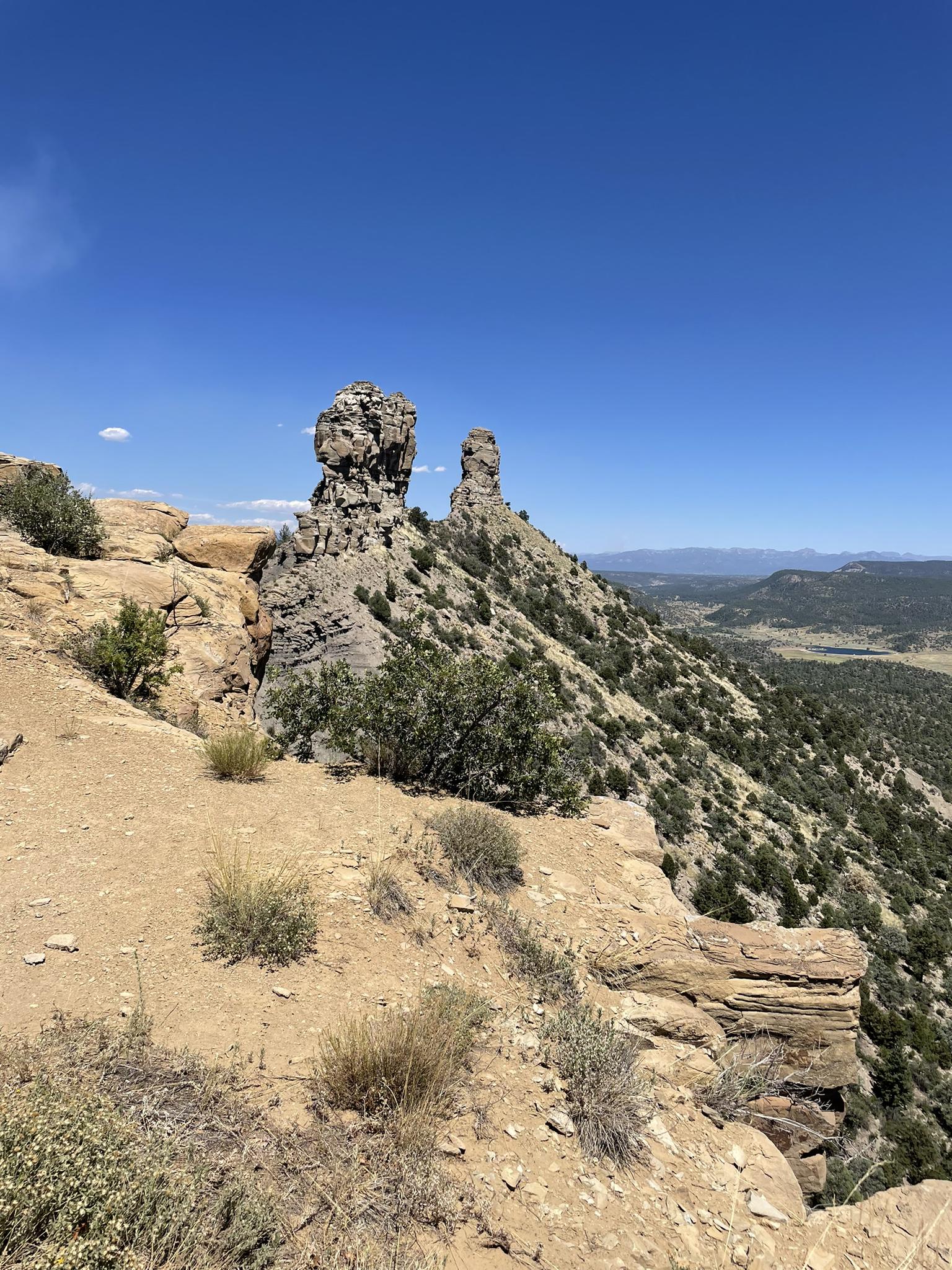Two large rock formations on a sunny, arid hillside overlooking a valley.
