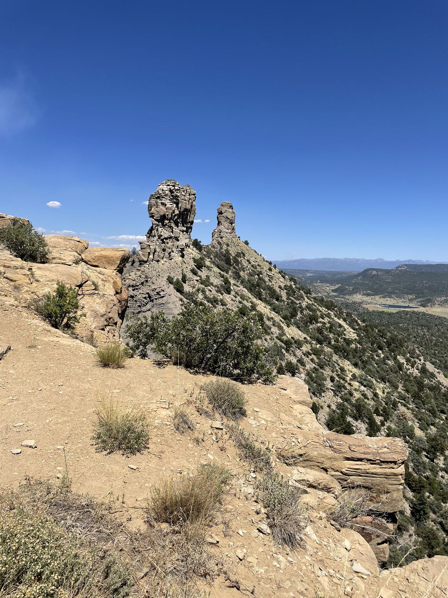 Two large rock formations on a sunny, arid hillside overlooking a valley. - Great House Pueblo Trail