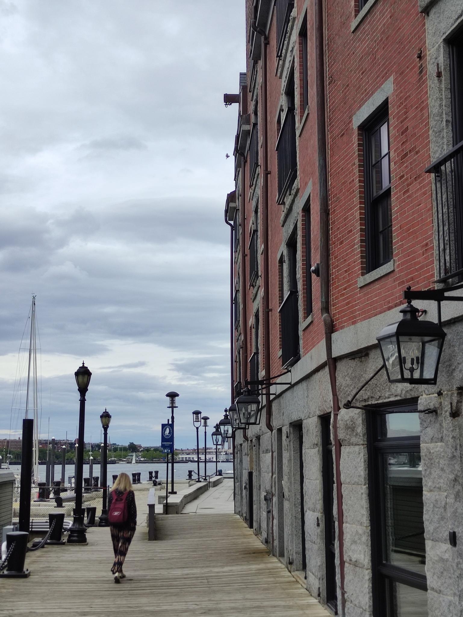 Woman walking on a wooden boardwalk next to a brick building on a cloudy day.