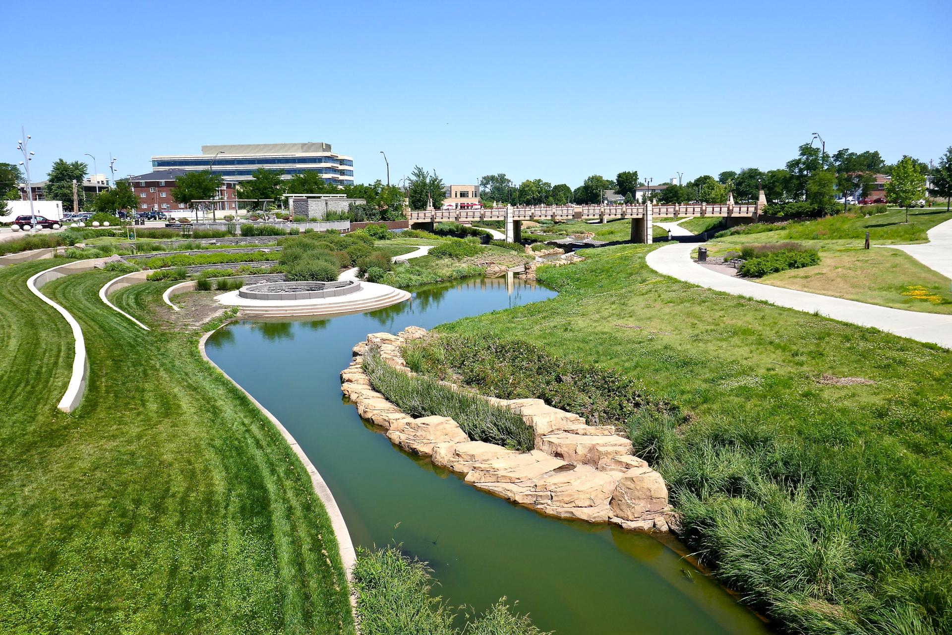 A winding river flows through a modern park with green lawns and bridges.