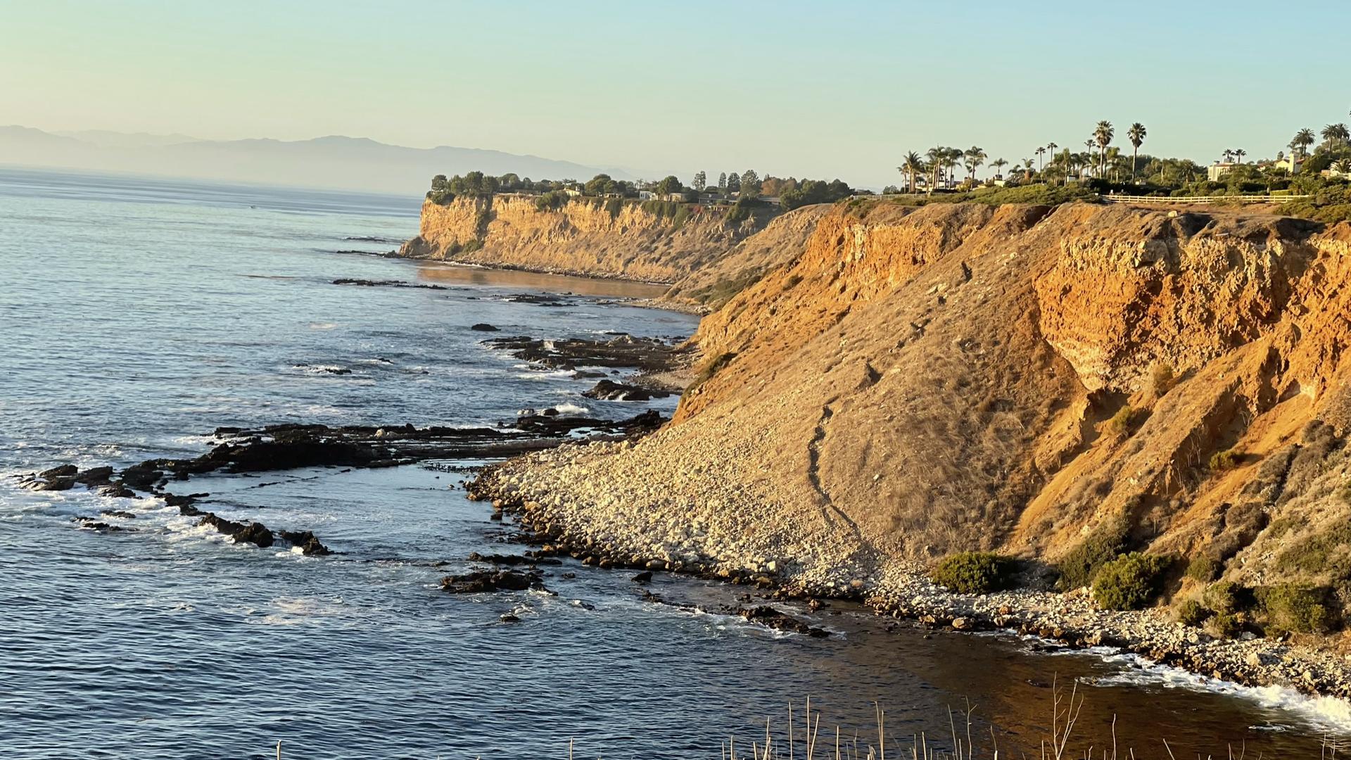 Rocky coastline with steep cliffs and calm ocean in warm evening light.