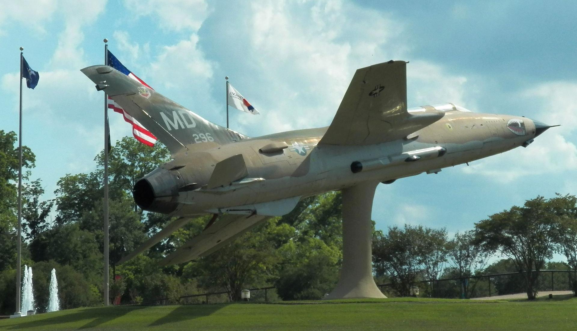 A military jet on a pedestal under a partly cloudy sky.