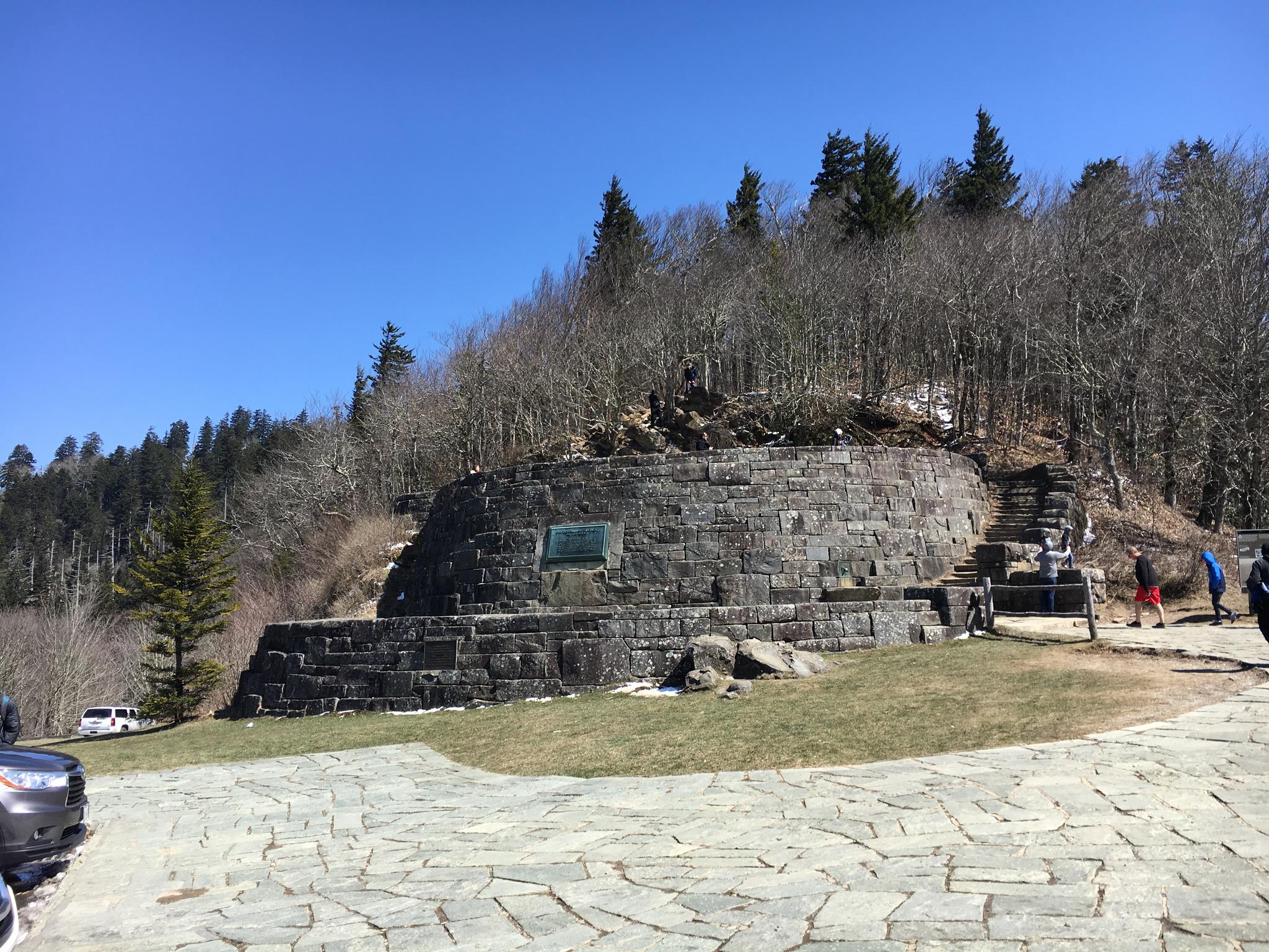 Large stone monument on a hill with bare trees under a sunny sky.