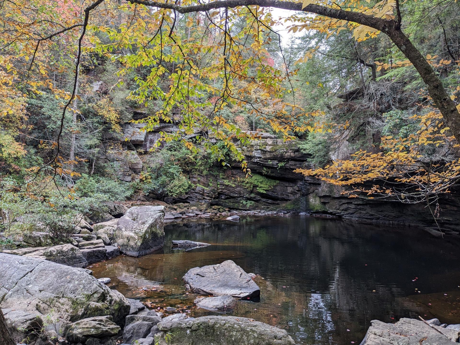 Serene dark pool surrounded by rocky cliffs and vibrant autumn trees.