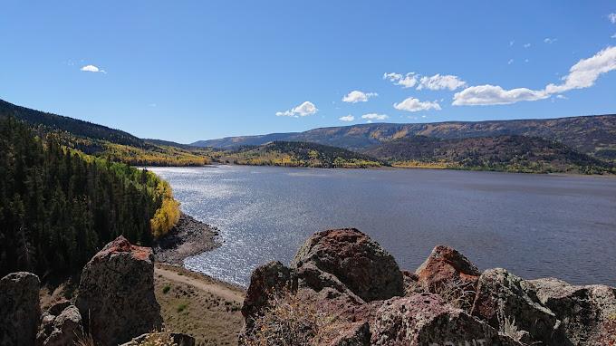 Scenic lake surrounded by forested hills with autumn colors under a bright sky.