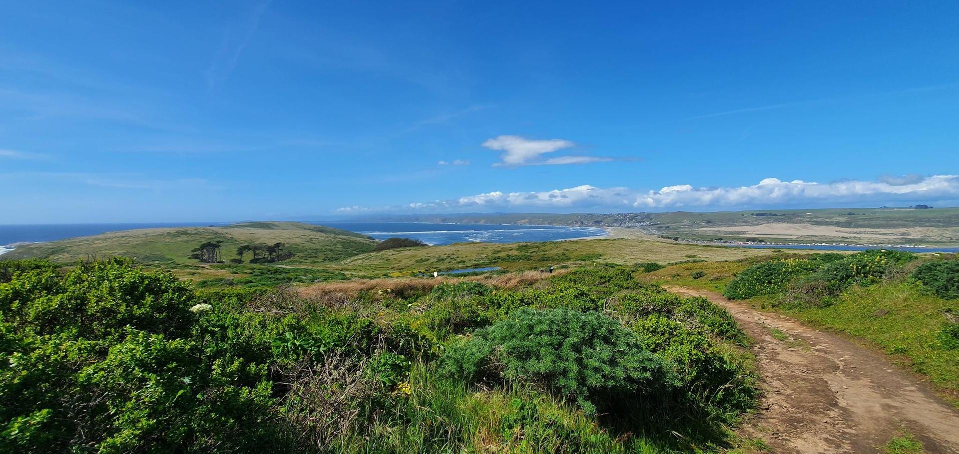 Panoramic view of green rolling hills, a dirt path, and distant ocean.