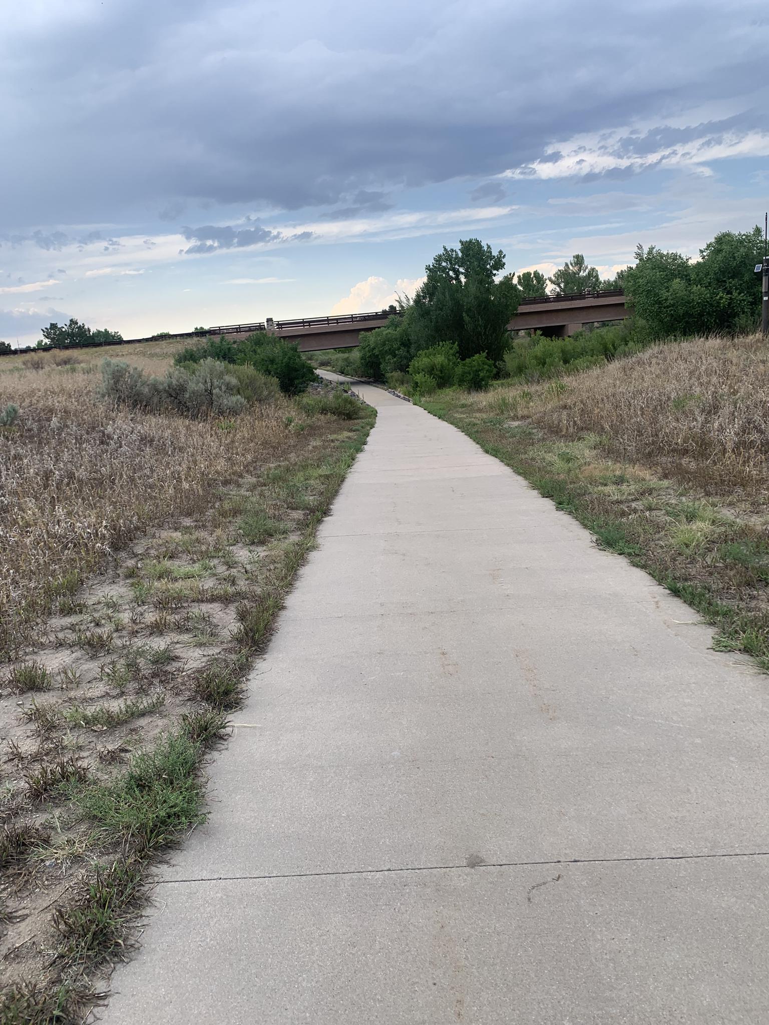 Paved path winding through dry grassy fields under an overcast sky.