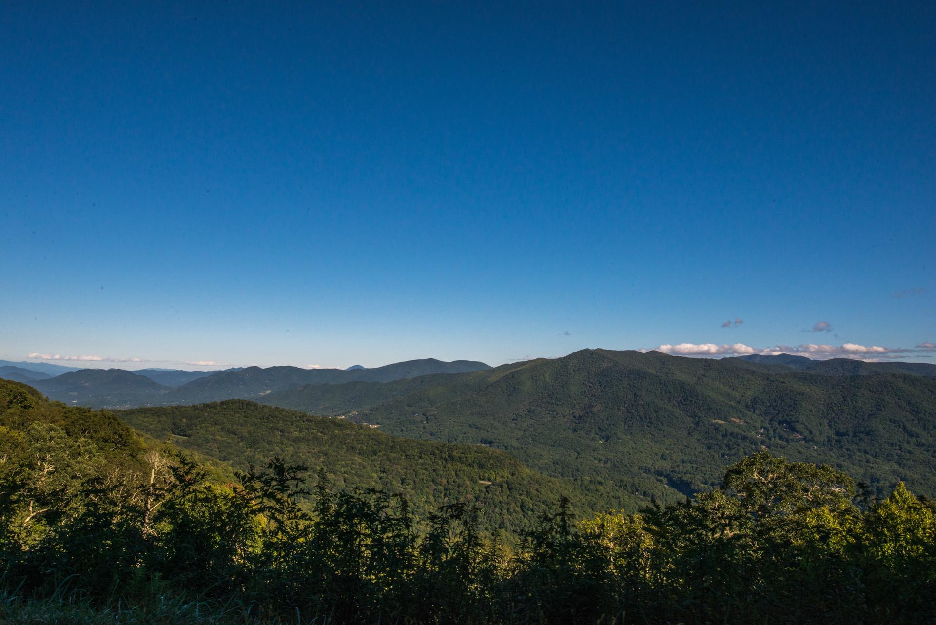 Expansive green forested mountains under a clear, bright blue sky.