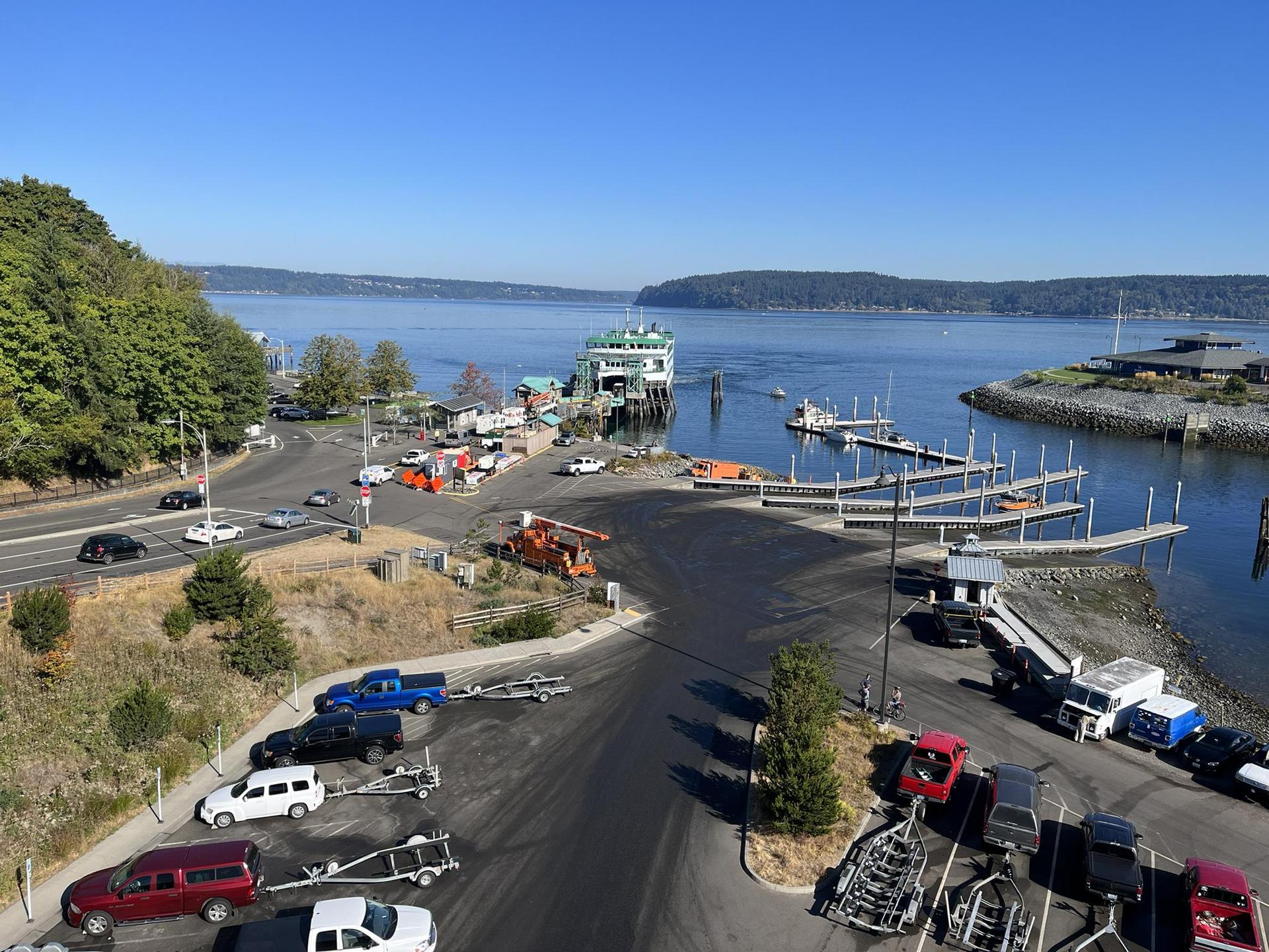 Sunny aerial view of a busy marina with a ferry, boats, and cars.