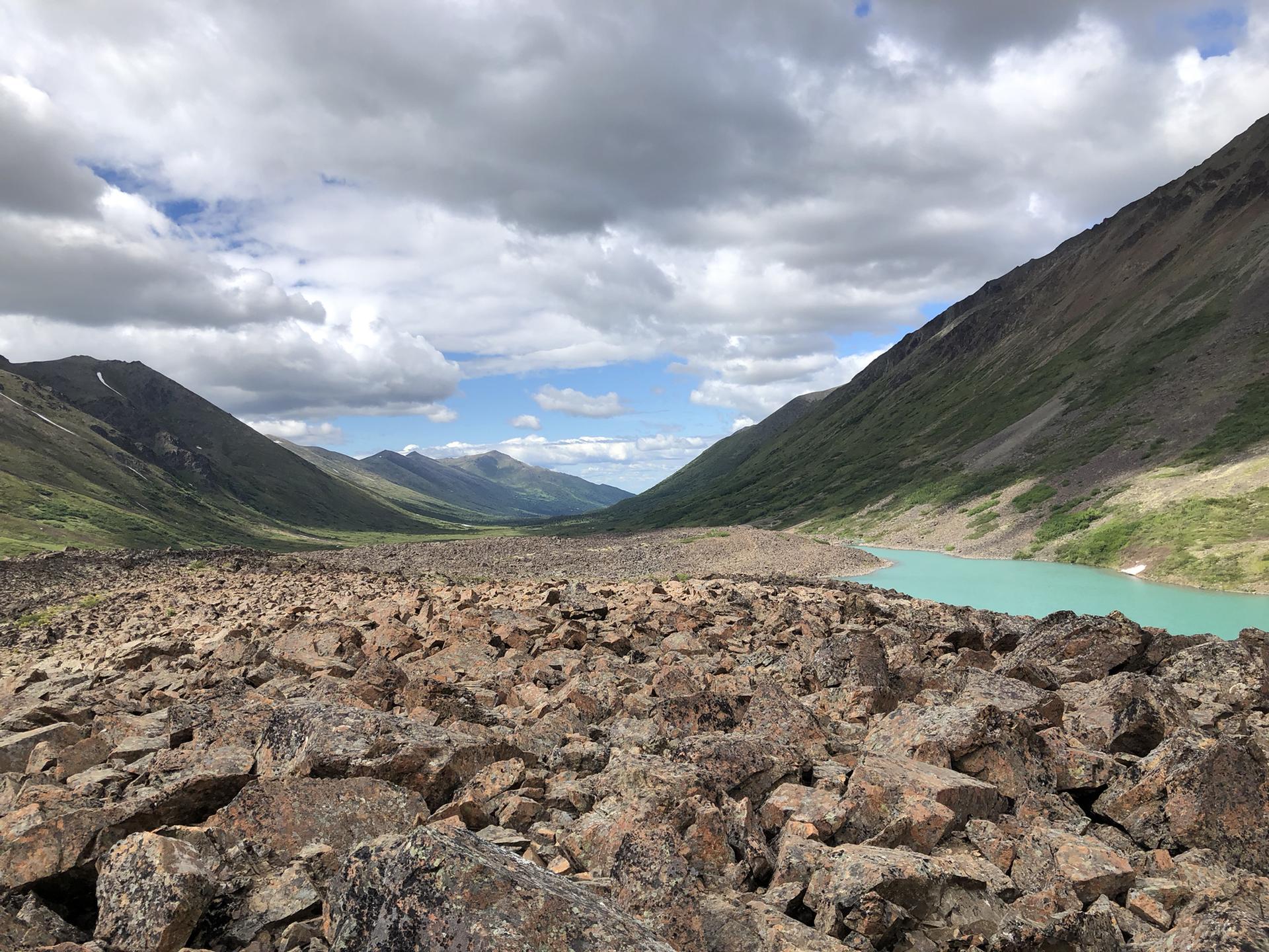 Vast rocky valley with a turquoise lake under a cloudy sky.