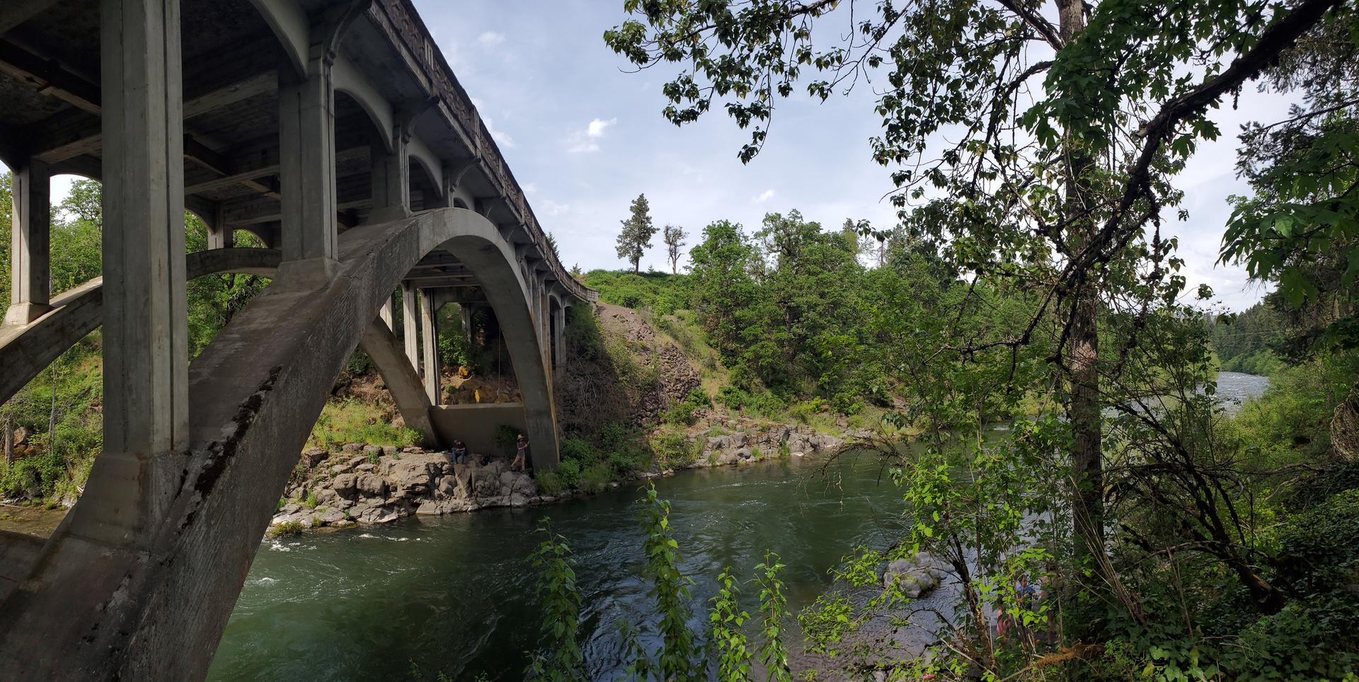 Concrete arch bridge over a river, surrounded by green trees.