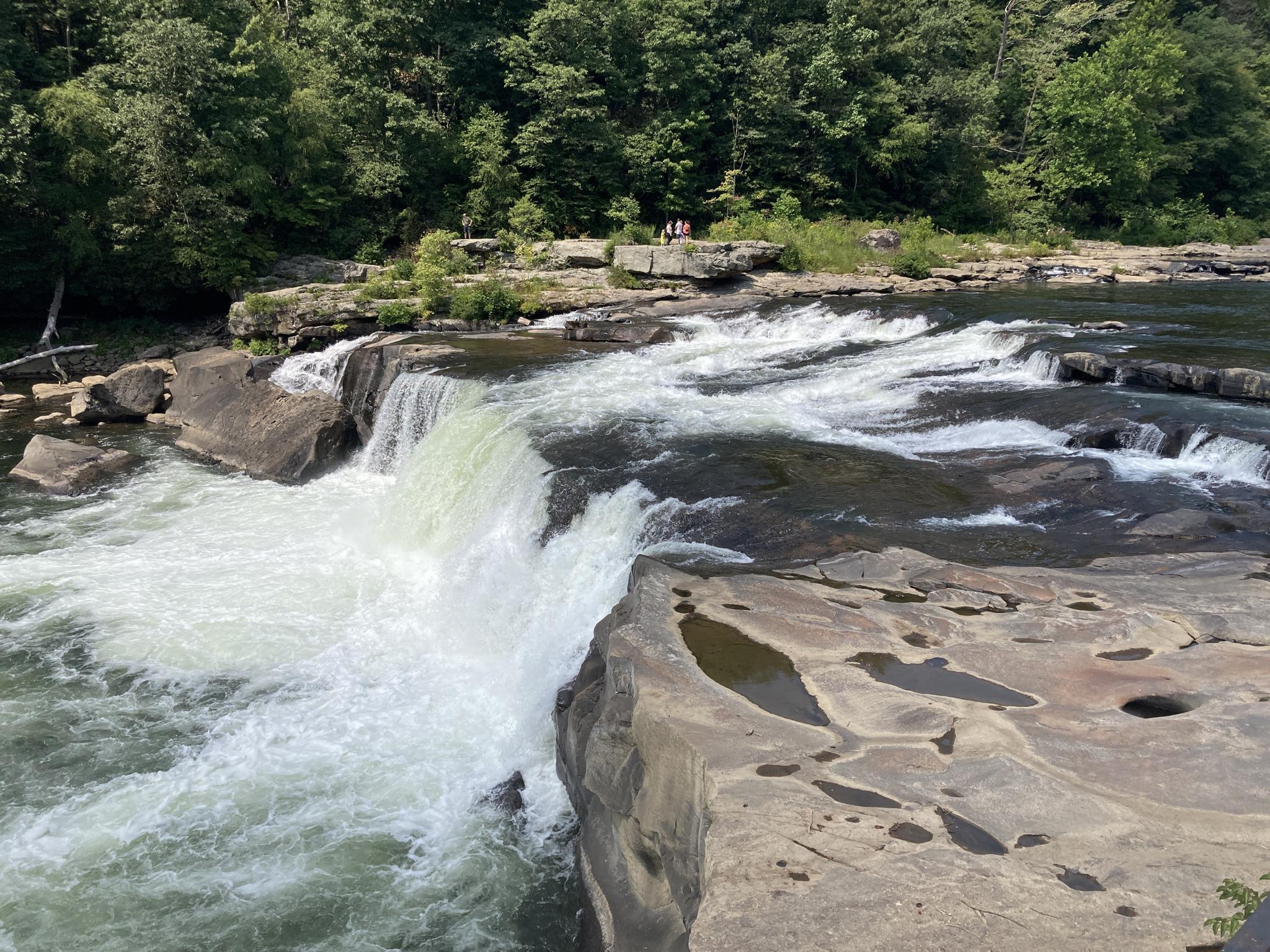 Close-up of a powerful waterfall over dark rocks, with distant people.
