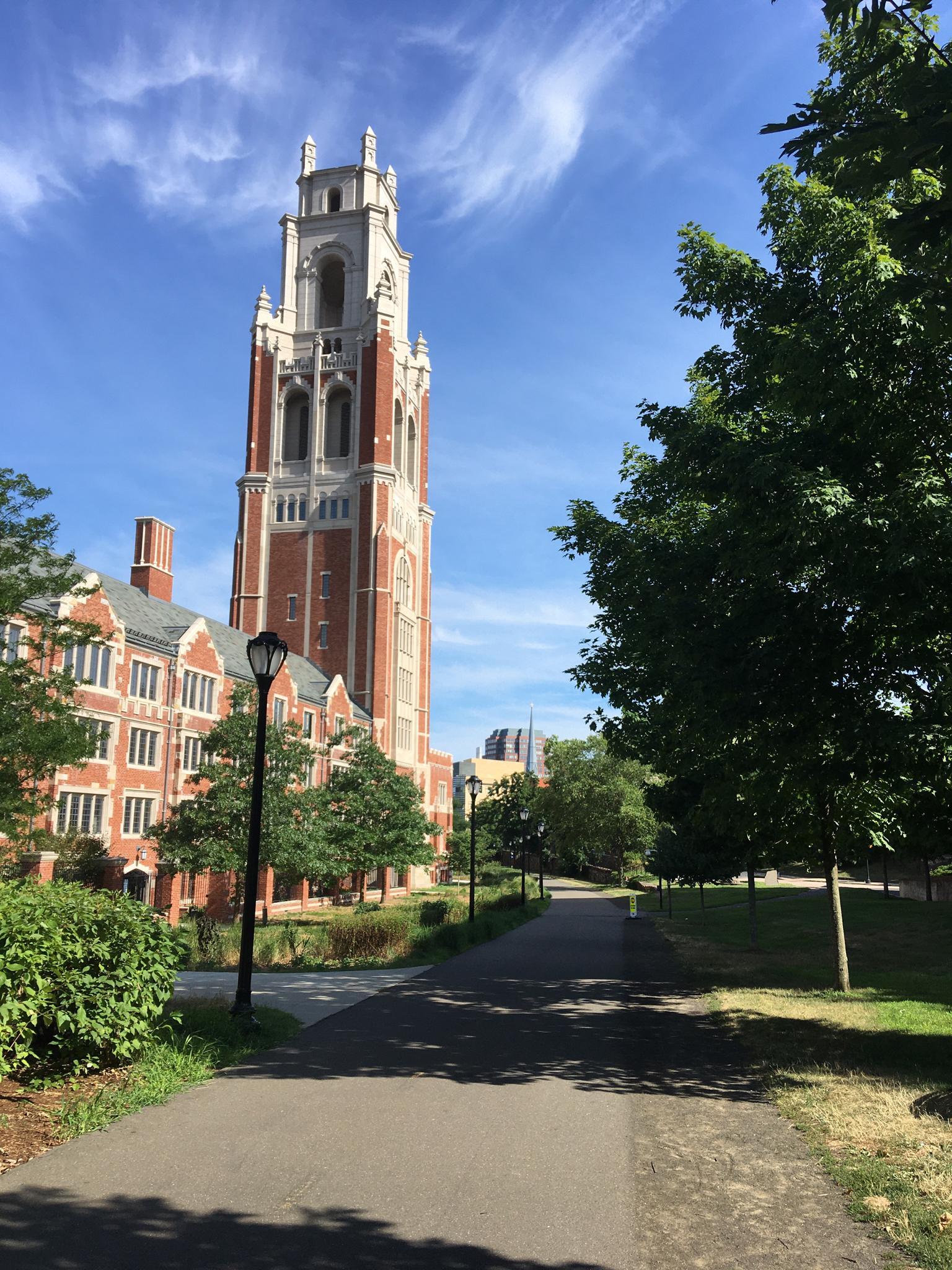 Tall brick tower building next to a paved path on a sunny day.