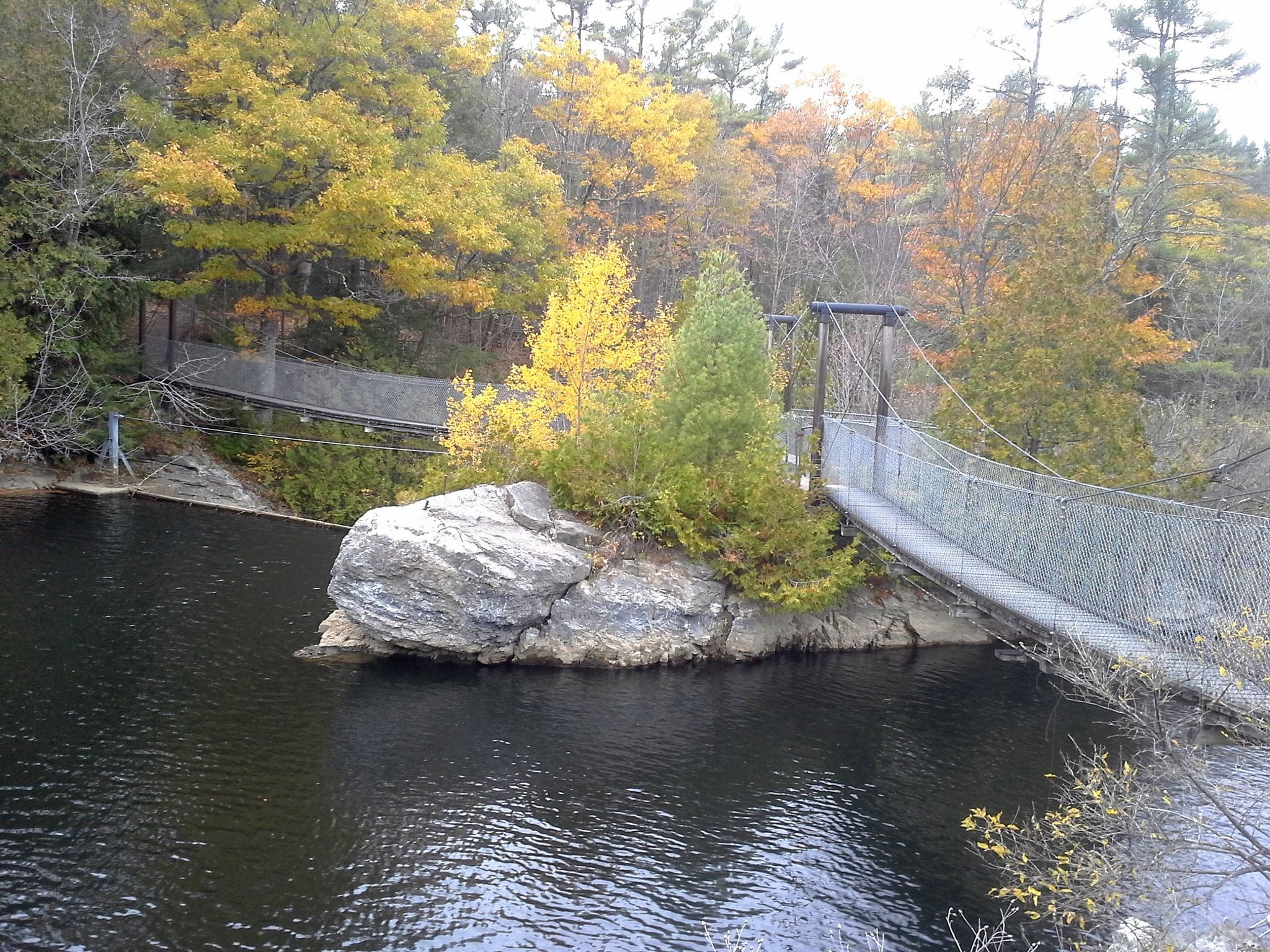 Two suspension bridges over dark water, with autumn trees and a rocky island. - Trail Around Middlebury: Otter Creek Gorge