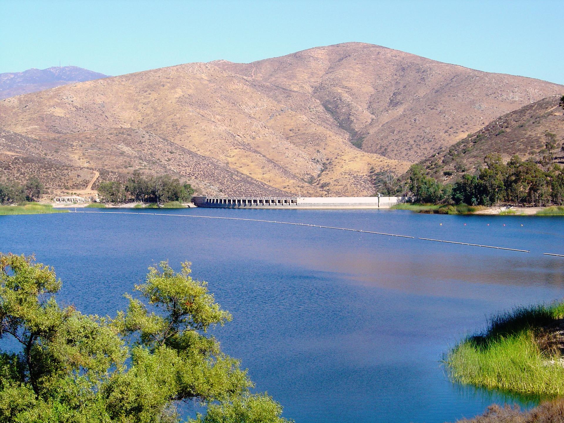 Blue lake with a dam, surrounded by dry hills under bright daylight.