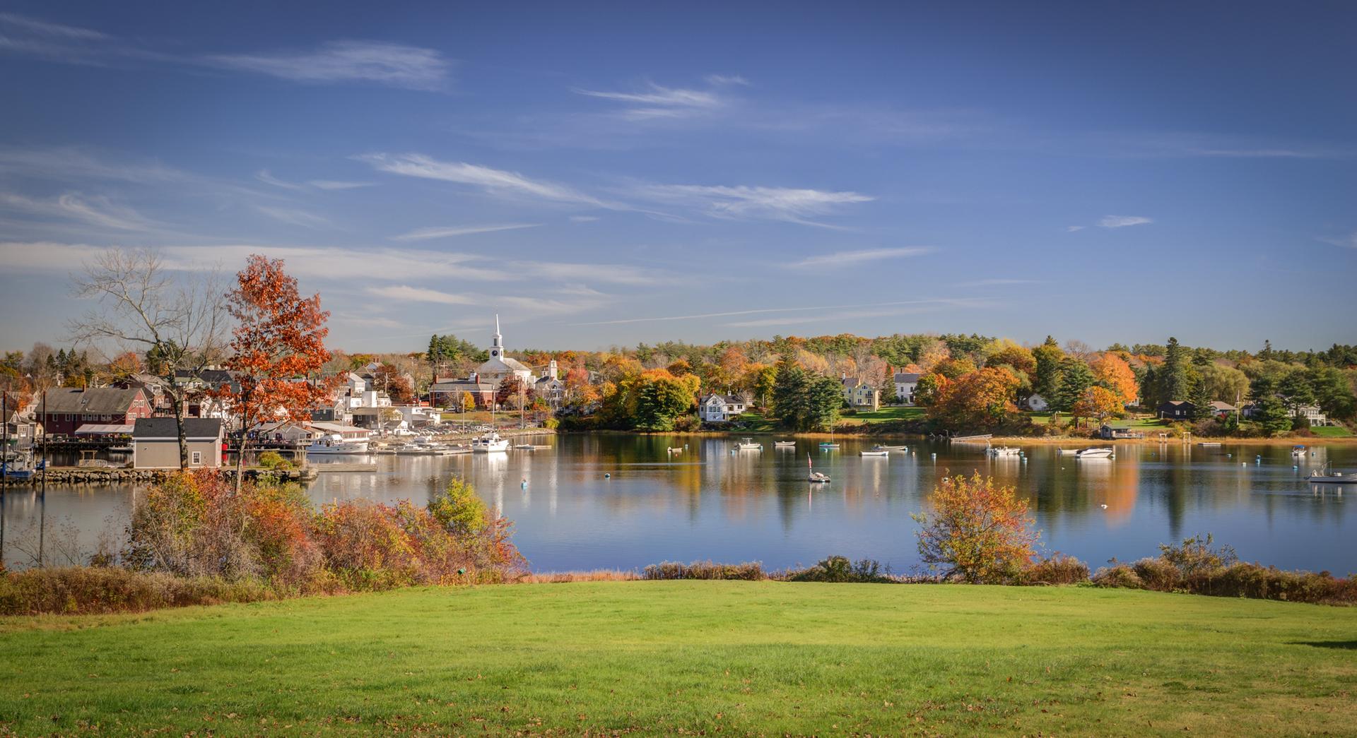 Scenic lake with a town and colorful autumn trees under a blue sky.