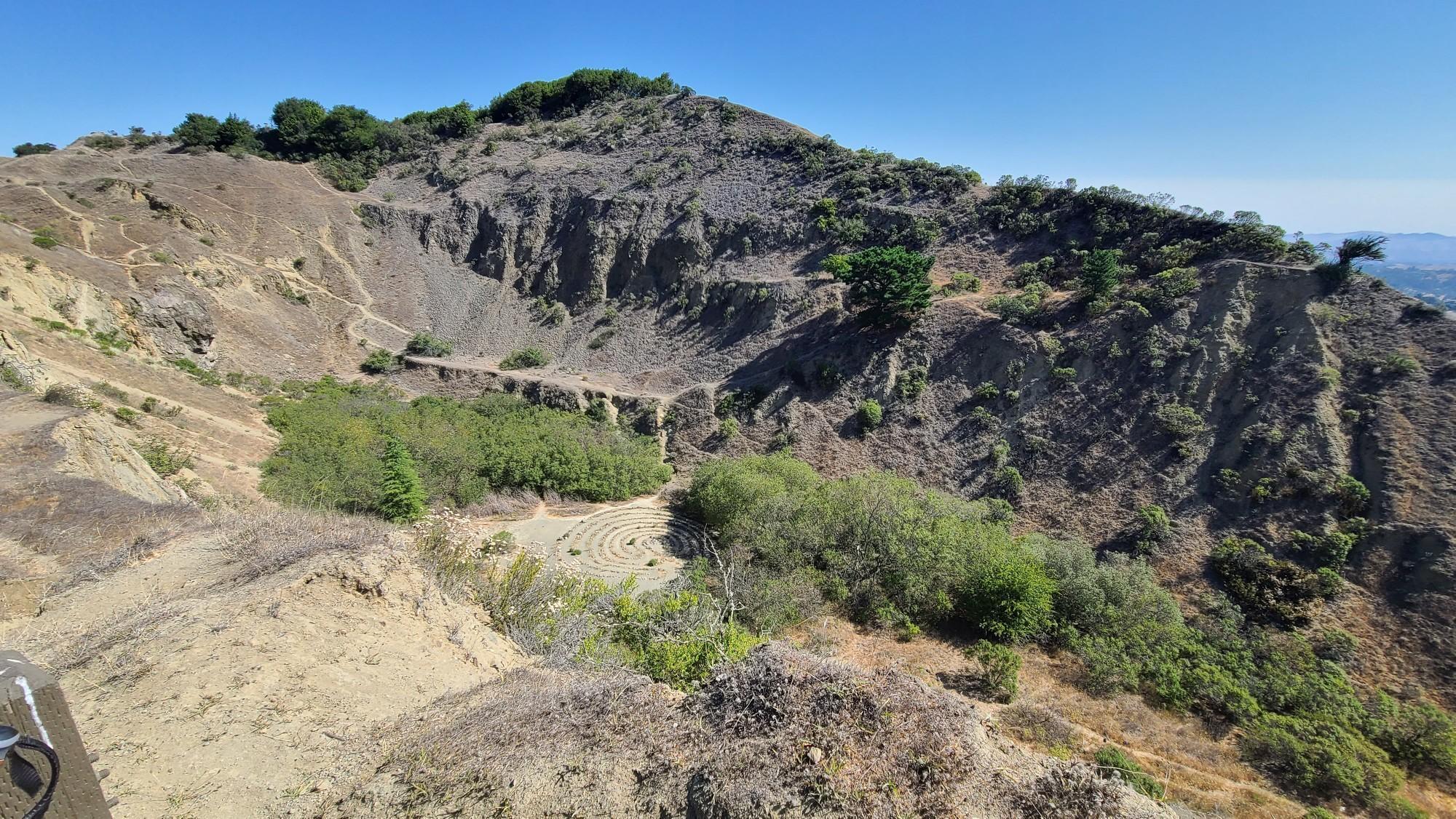 Steep, rocky hillsides with patches of green foliage under a clear blue sky.