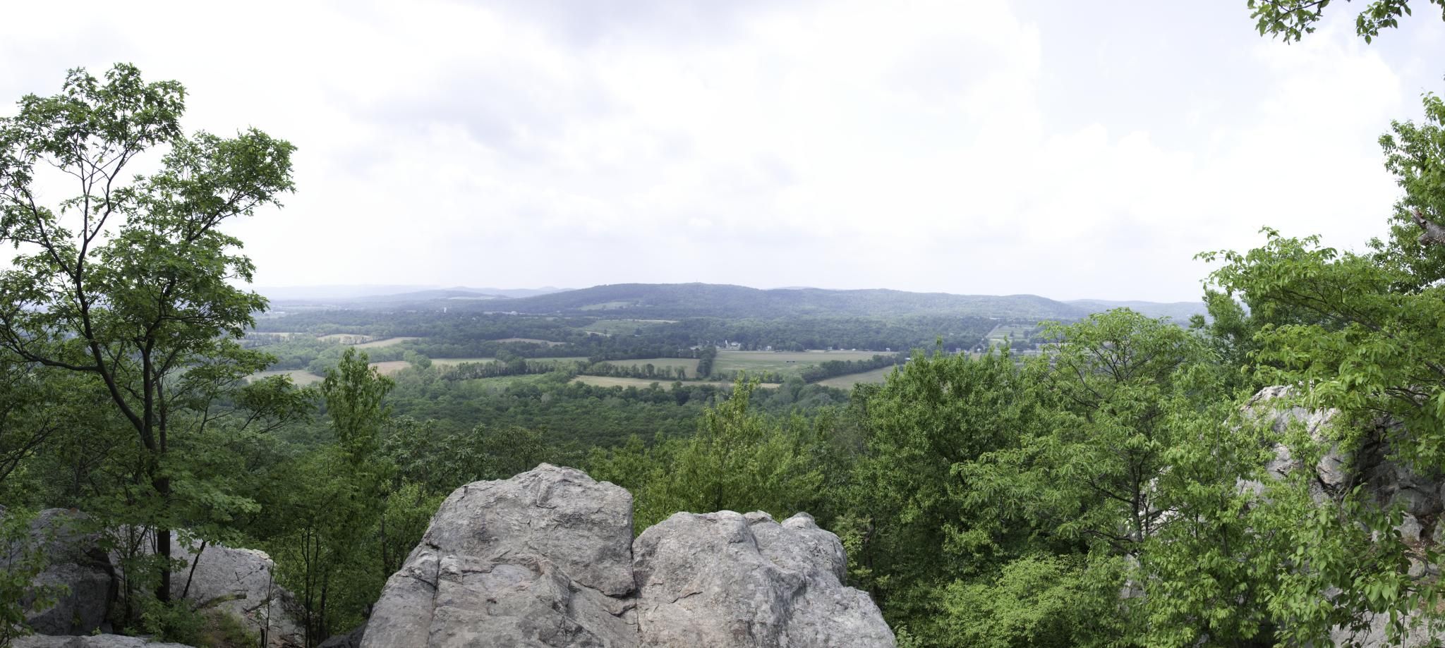 Panoramic view from rocky outcrop over green forests and distant hills under cloudy sky. - Orange Trail