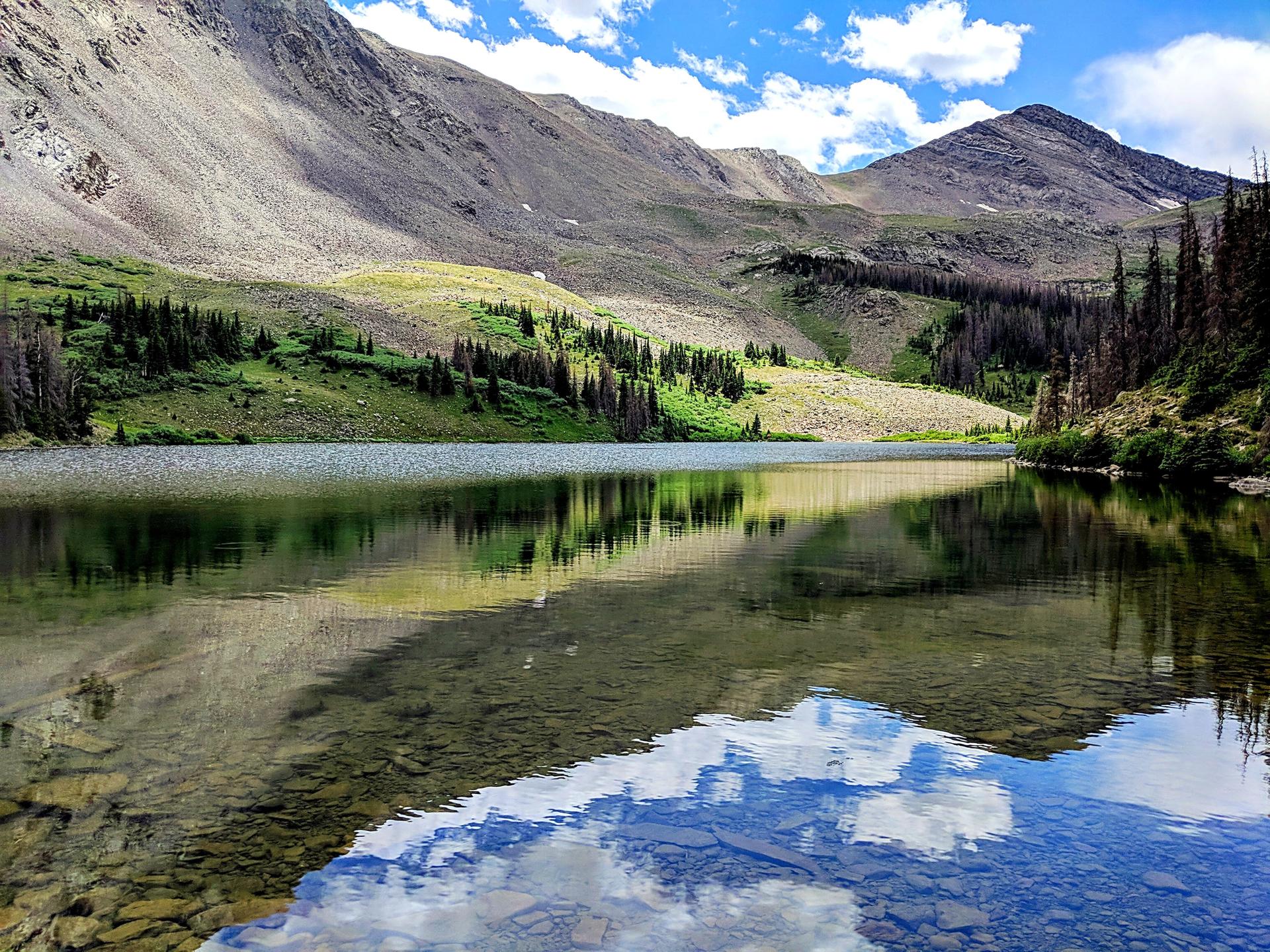Clear mountain lake reflecting blue sky and rocky peaks on a sunny day.