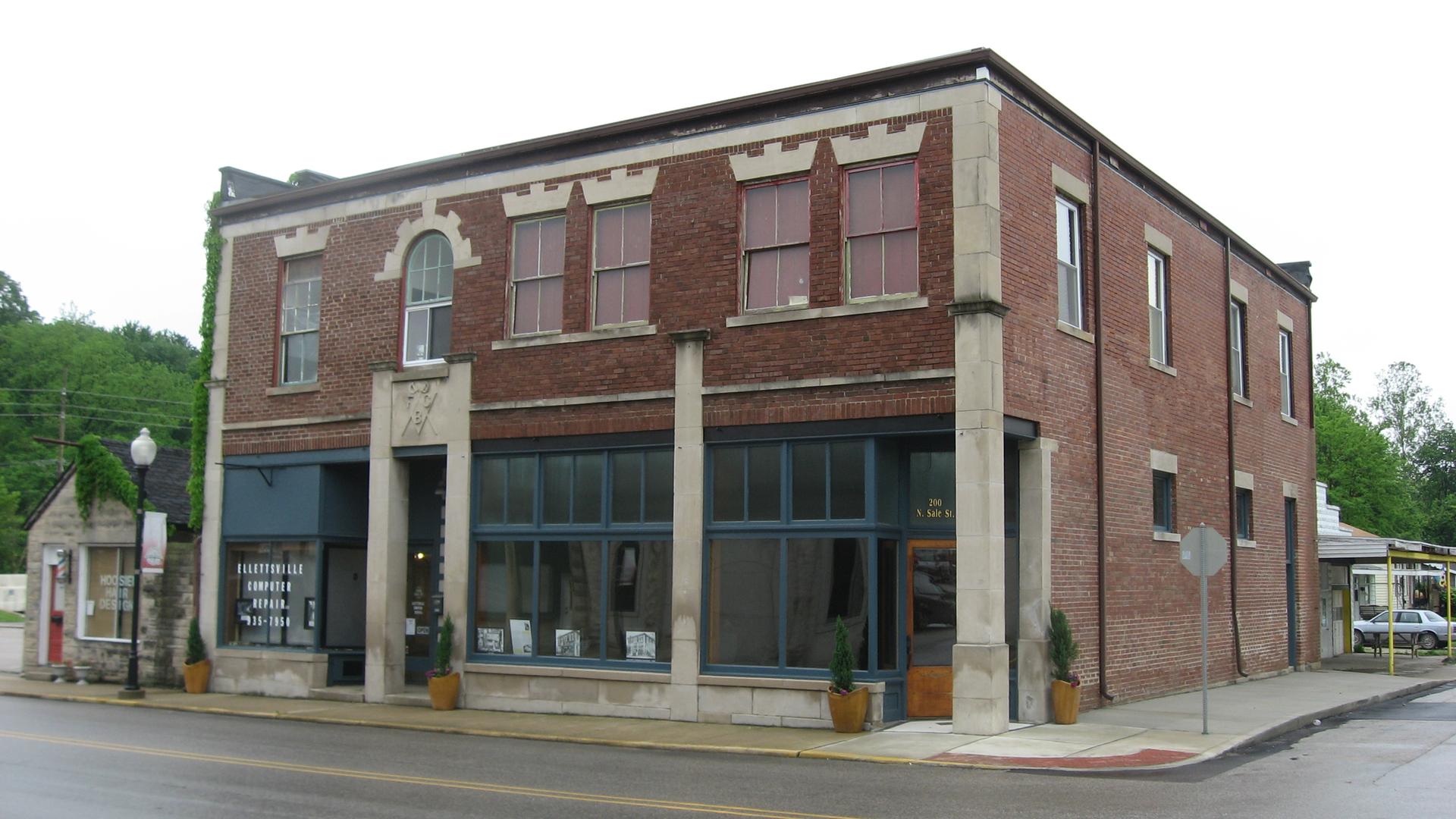 A two-story brick building with large windows on a street under an overcast sky.