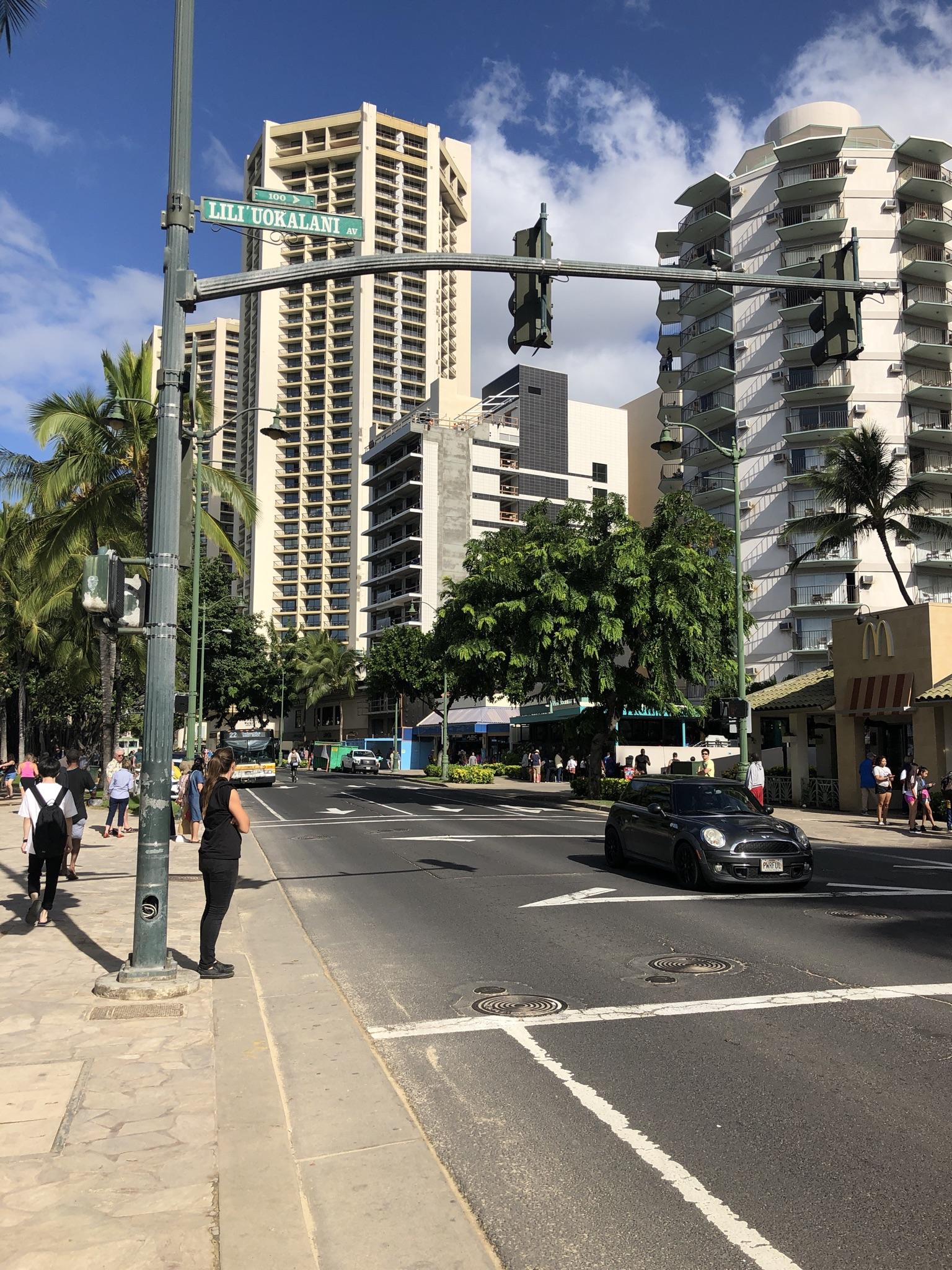 Busy city street with tall buildings, people walking, and a car.
