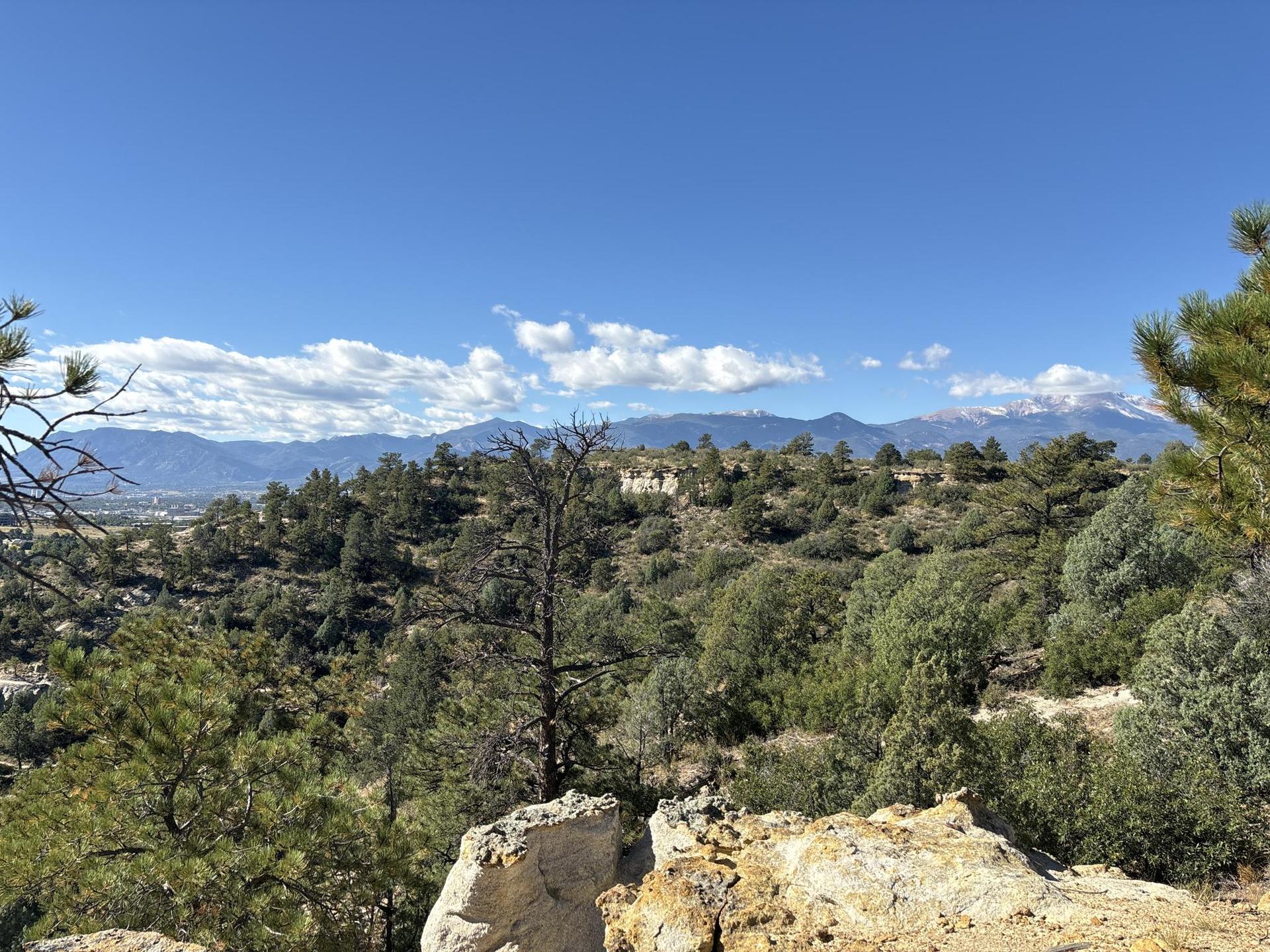 A wide view of green forested hills and distant mountains under a blue sky.