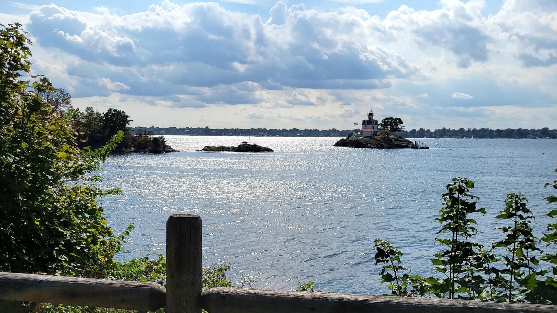A small lighthouse on a rocky island in a sparkling bay under cloudy skies.