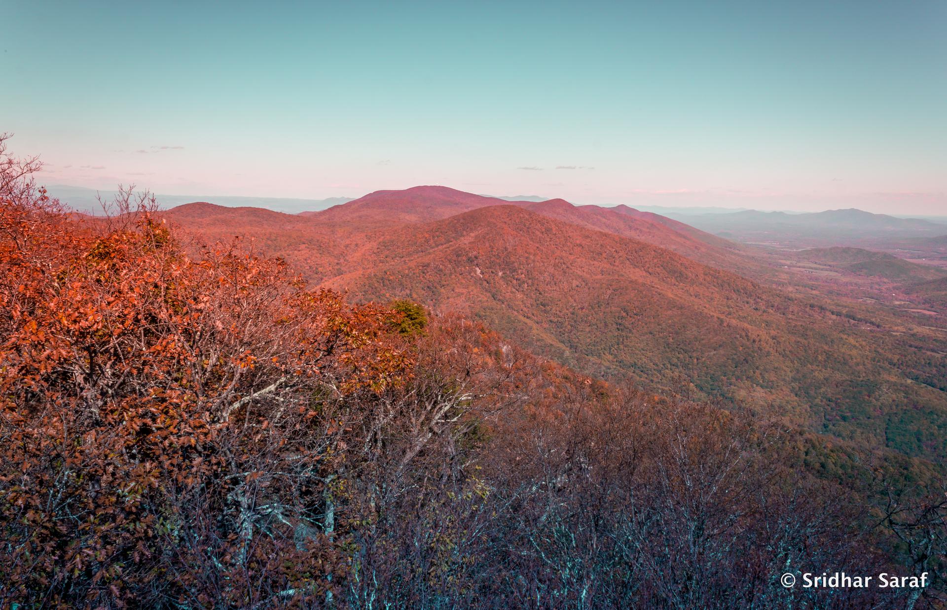 Autumn mountains with reddish foliage under a soft, clear sky at dusk.