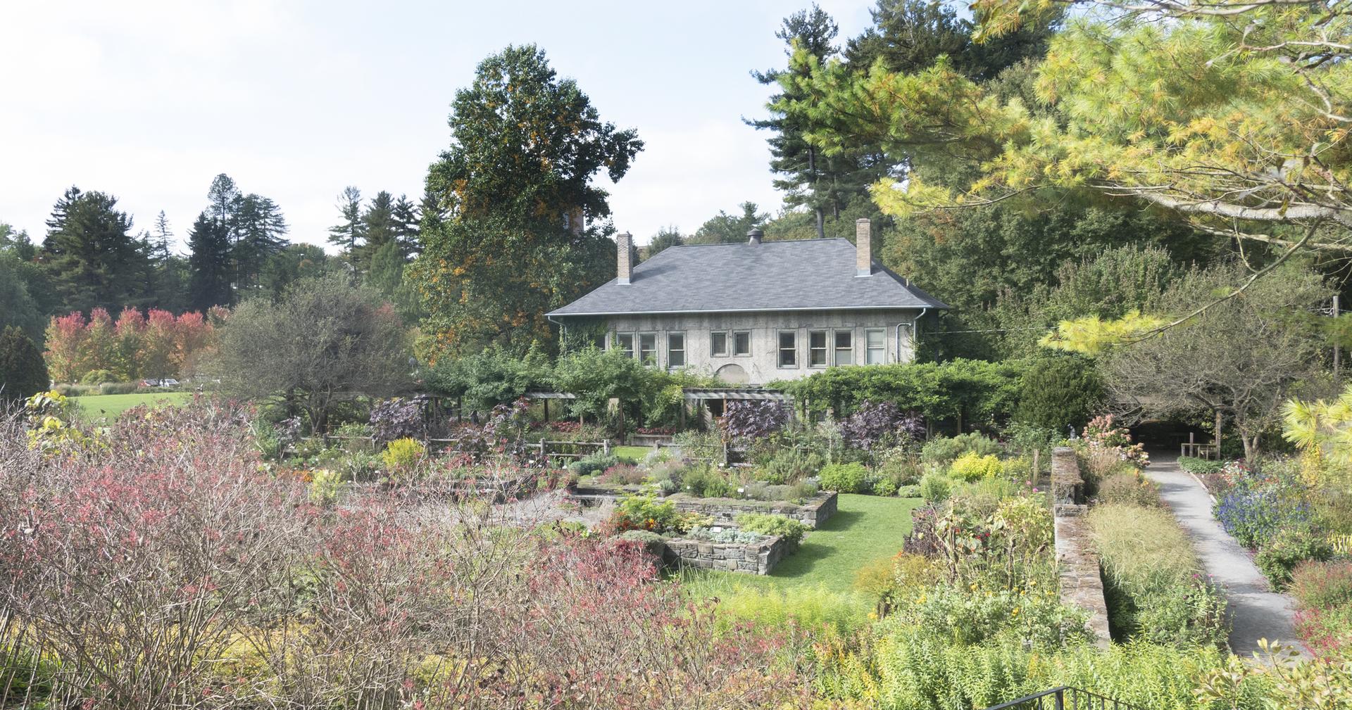 Historic stone house nestled in vibrant, multi-level gardens on a sunny day.