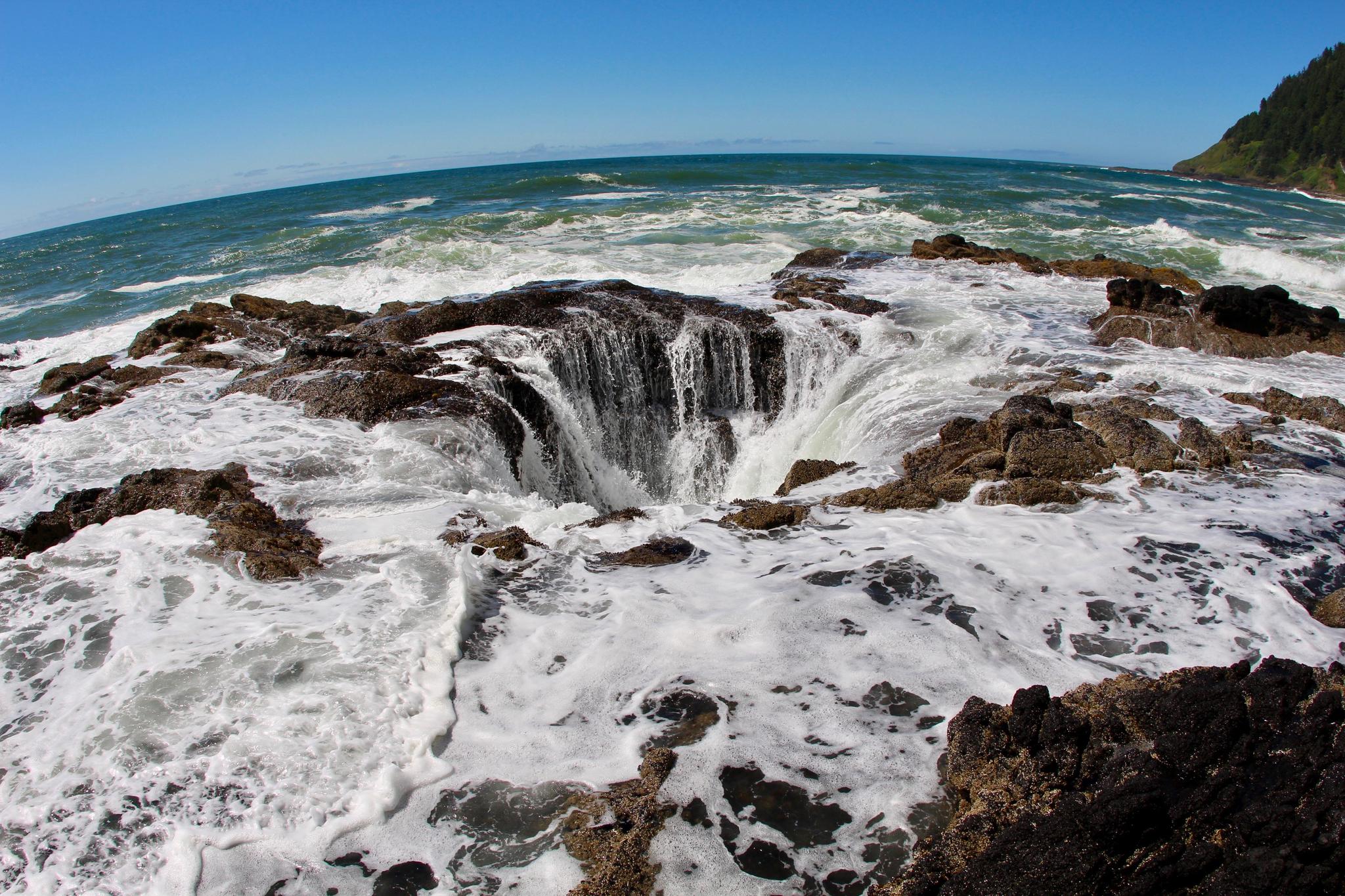 Powerful ocean waves crash into a large, circular rock formation.
