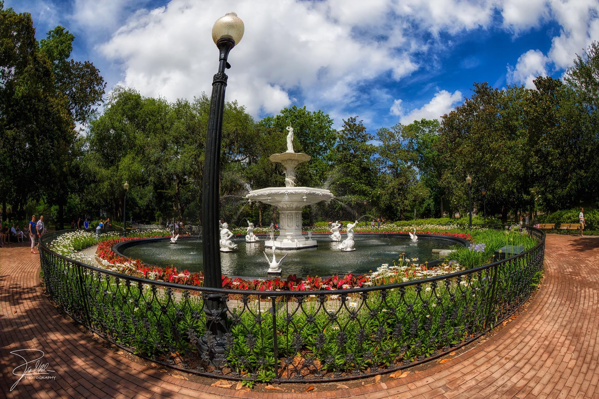Ornate white fountain with statues in a park on a cloudy day.