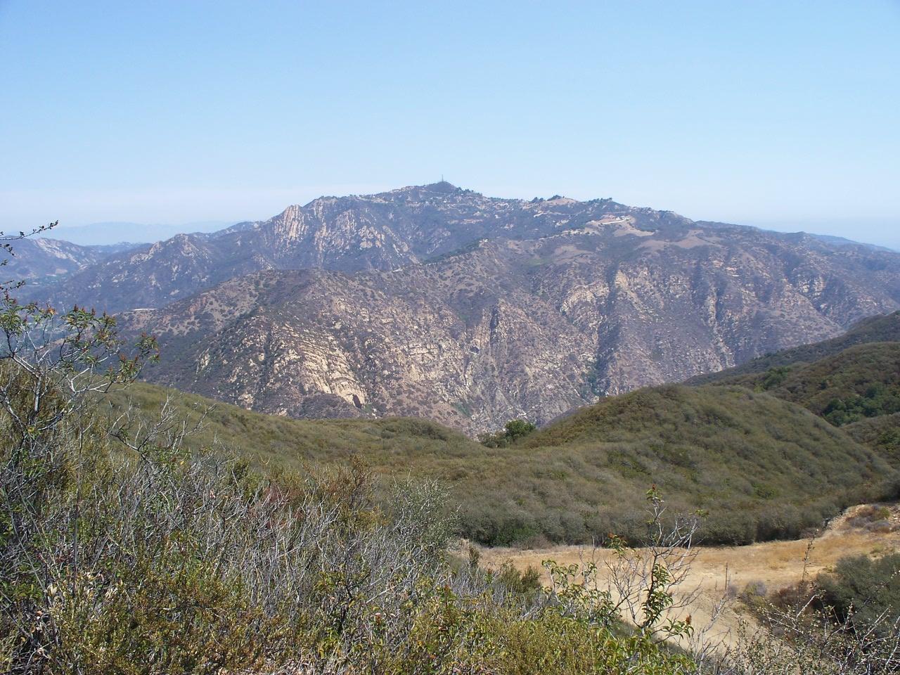 Expansive view of dry, rocky mountains and scrubland under a clear sky.