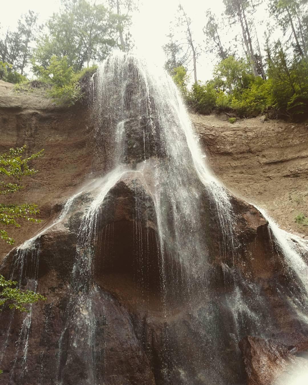 Powerful waterfall cascades down a tall rocky cliff with trees above.