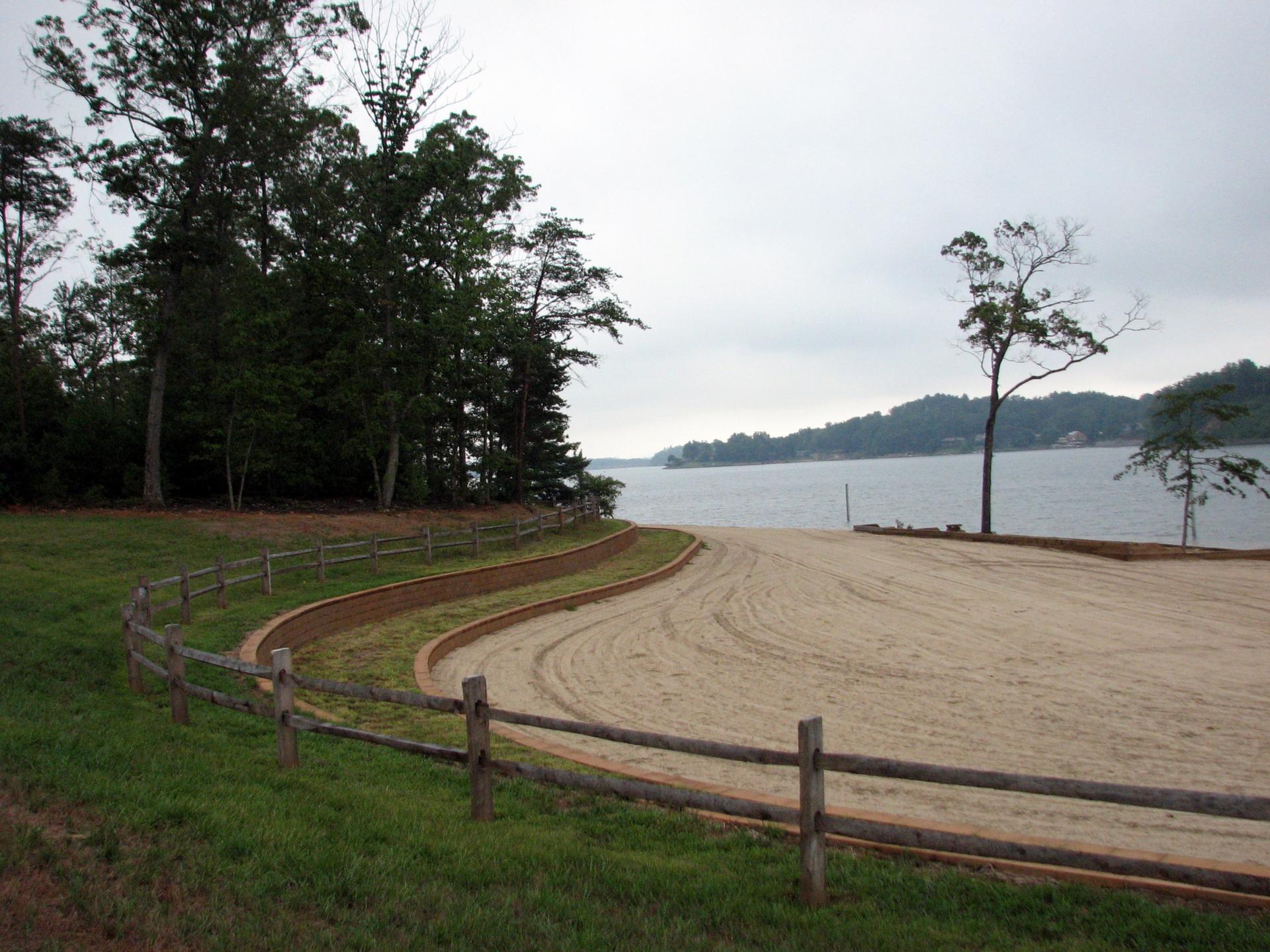 A sandy beach with a wooden fence borders a lake under an overcast sky.