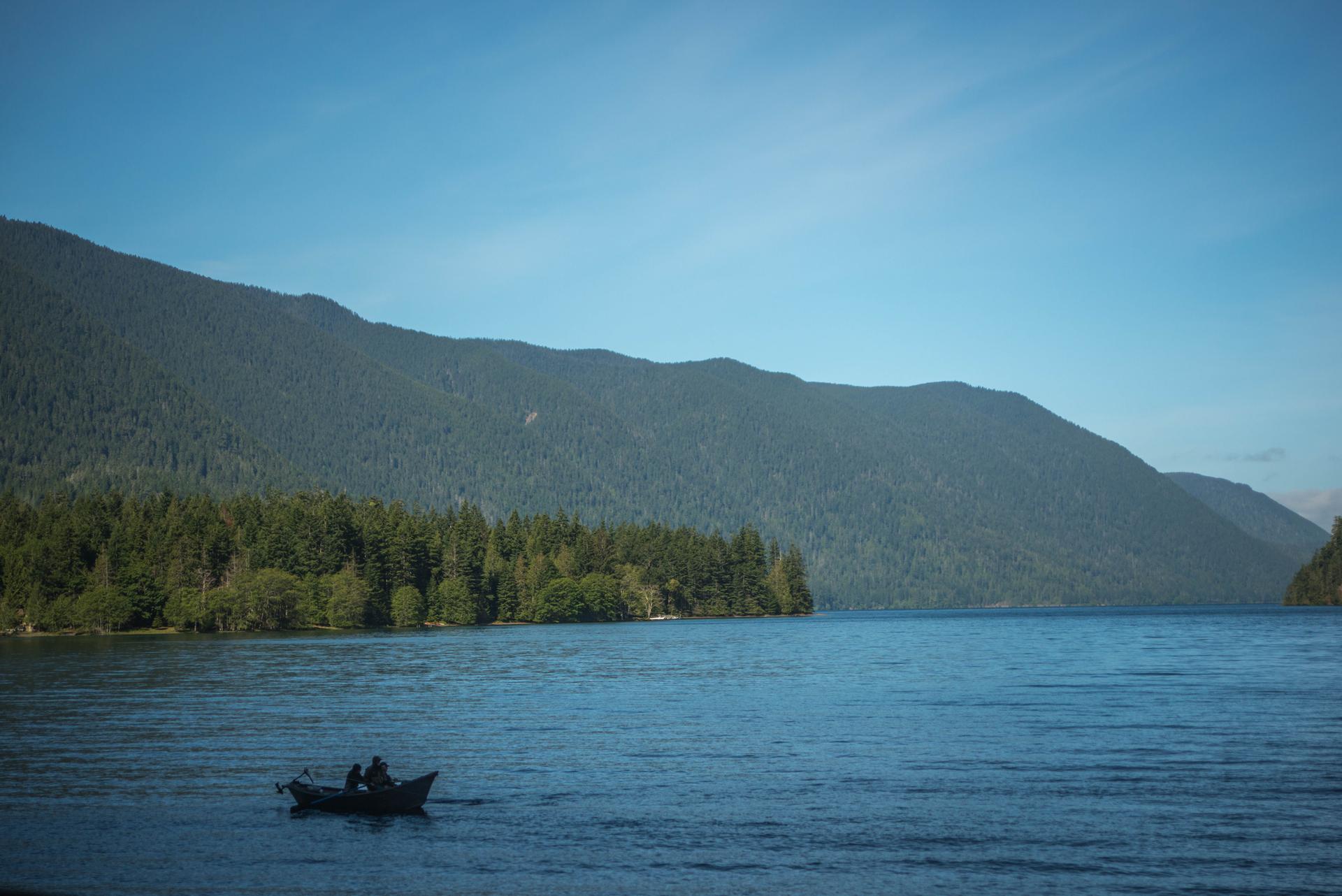 Two people in a small boat on a lake, forested mountains in background.