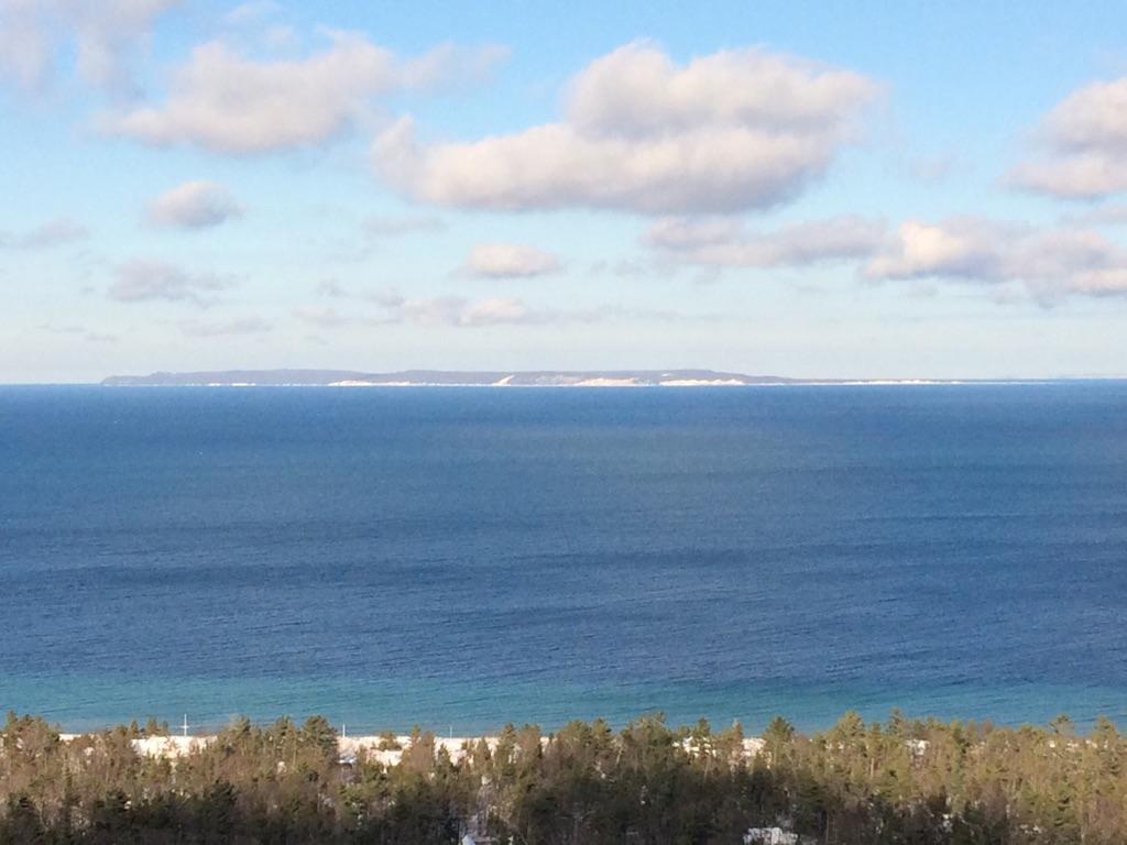 Expansive blue water, a distant snowy coastline, and a dark winter forest.