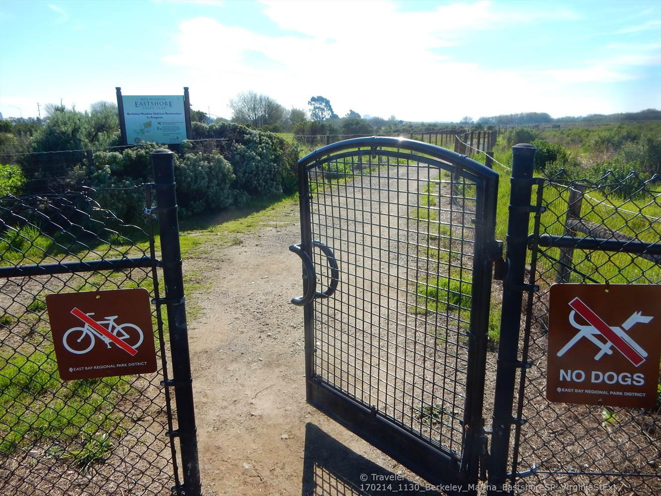An open metal gate with "no bikes" and "no dogs" signs on a dirt path.