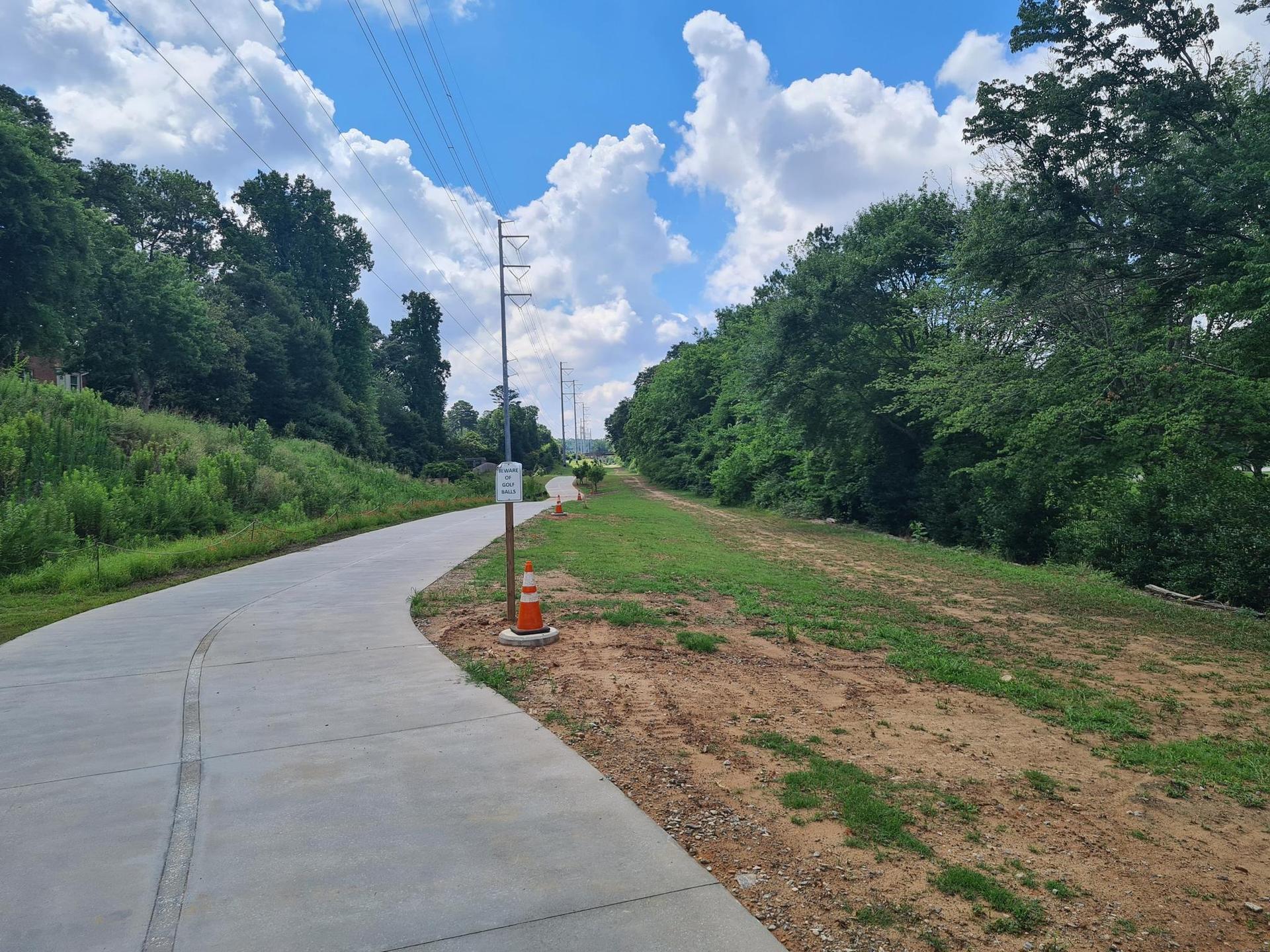 A winding paved path through green trees and grass under a cloudy sky.