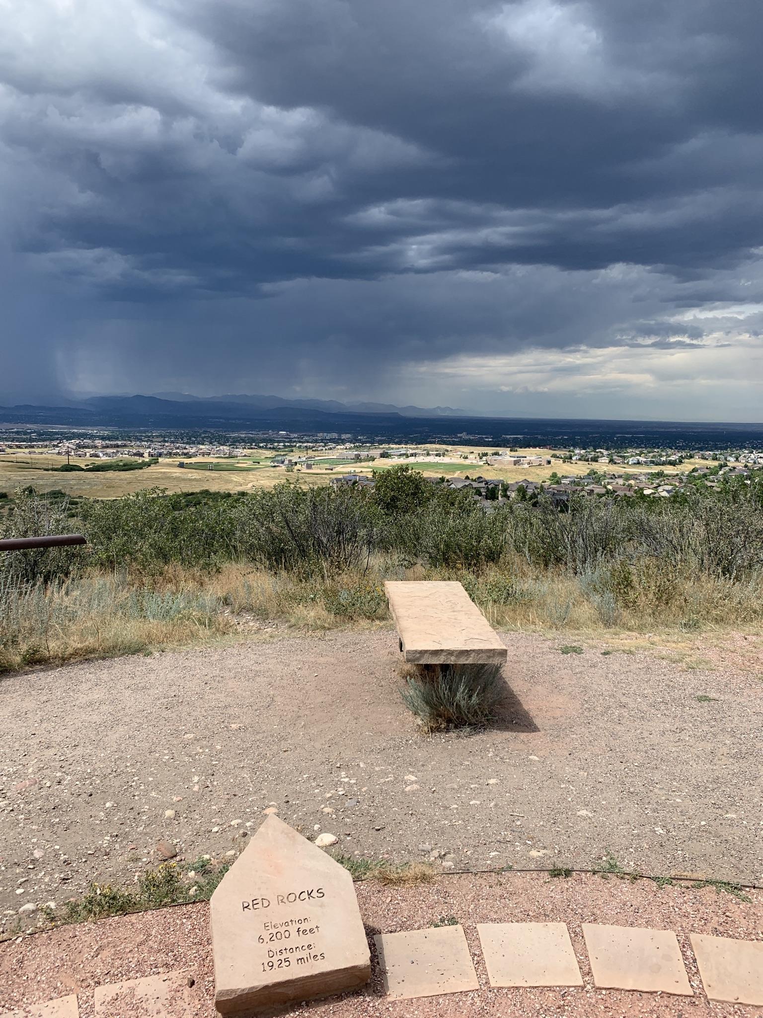 Stone bench and marker overlooking a valley under a dramatic, stormy sky.